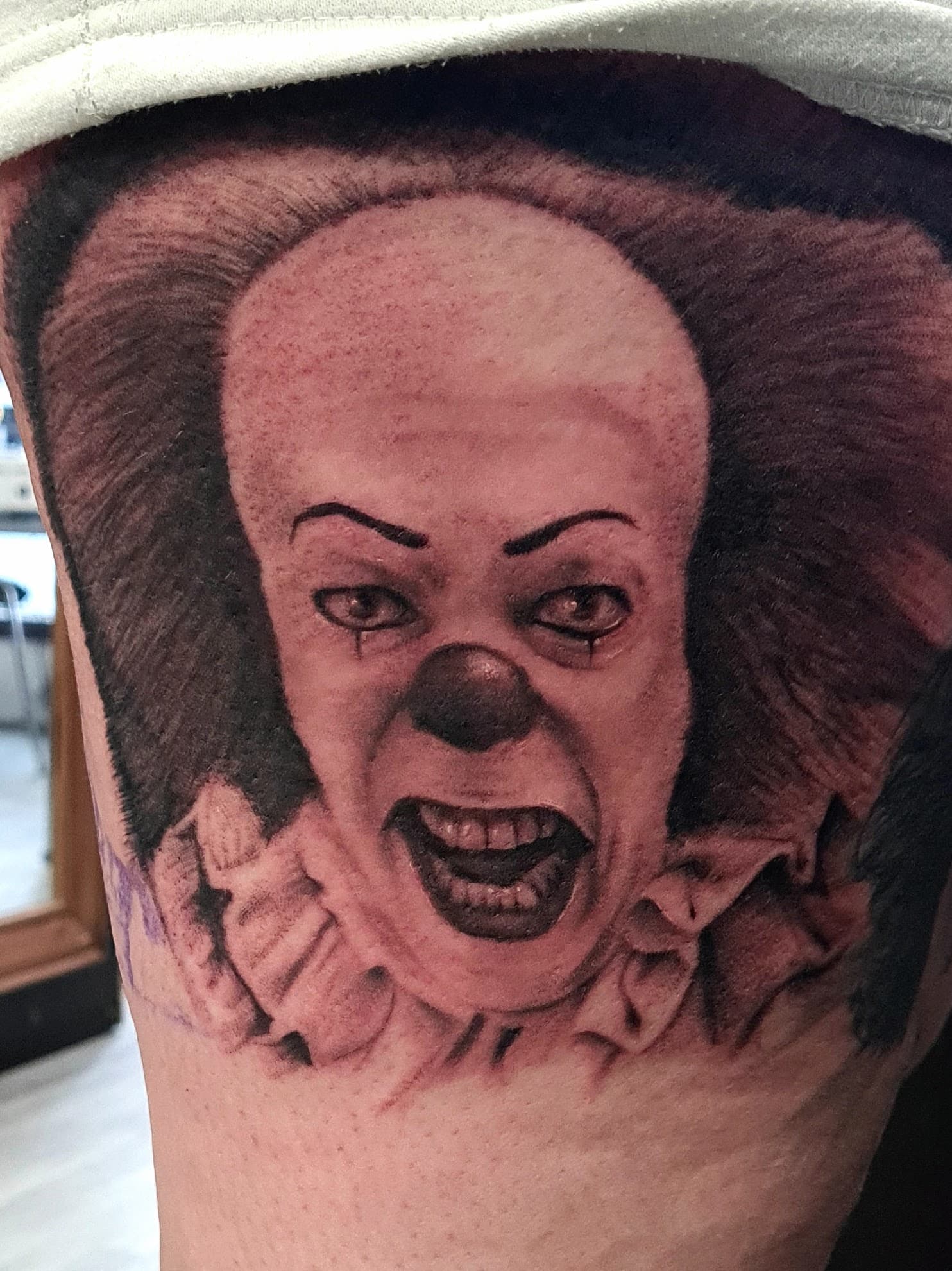 Black and grey realism tattoo of Pennywise the horror clown from IT on the thigh