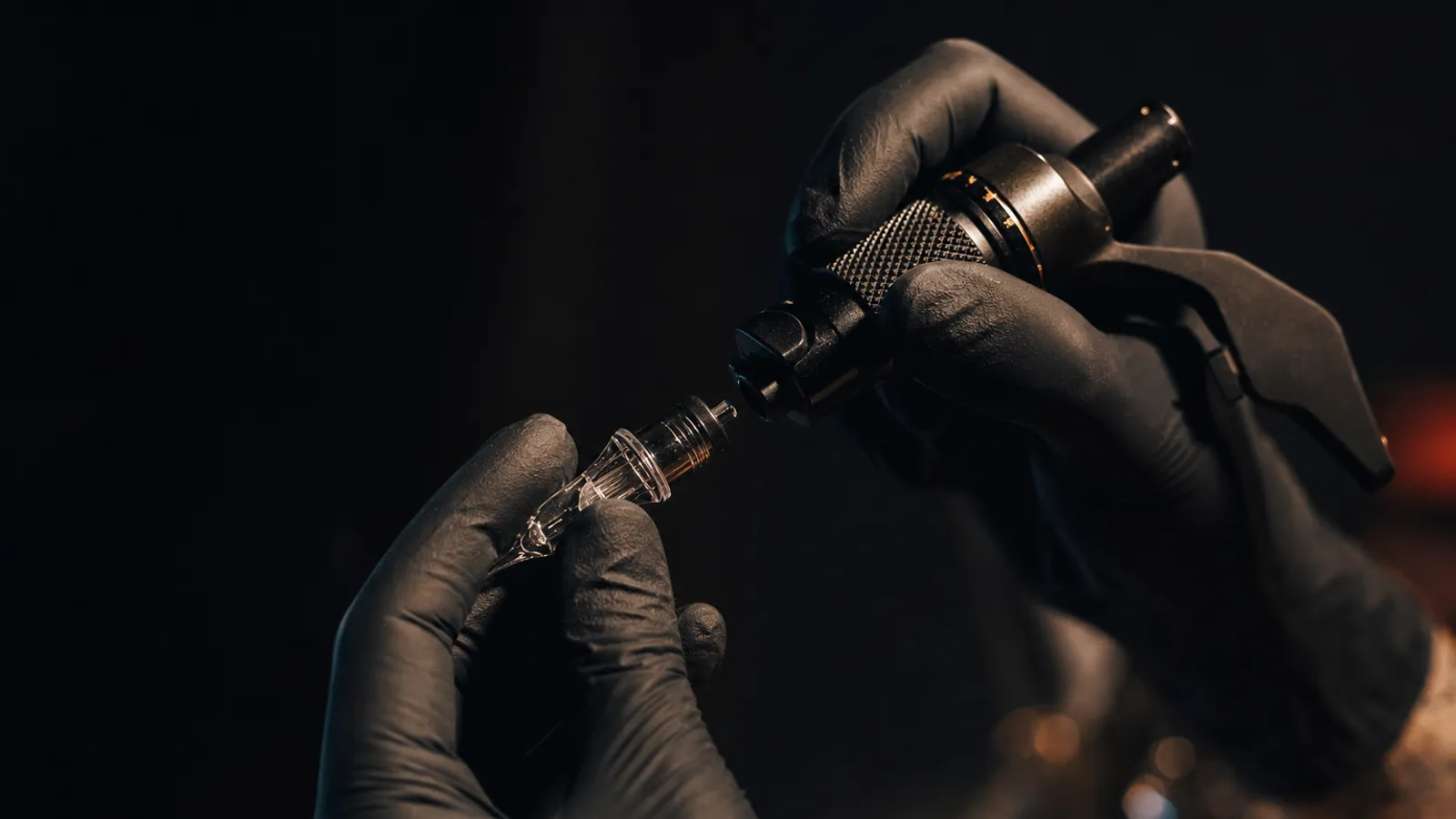 Gloved hands loading a sterile needle cartridge into a tattoo machine