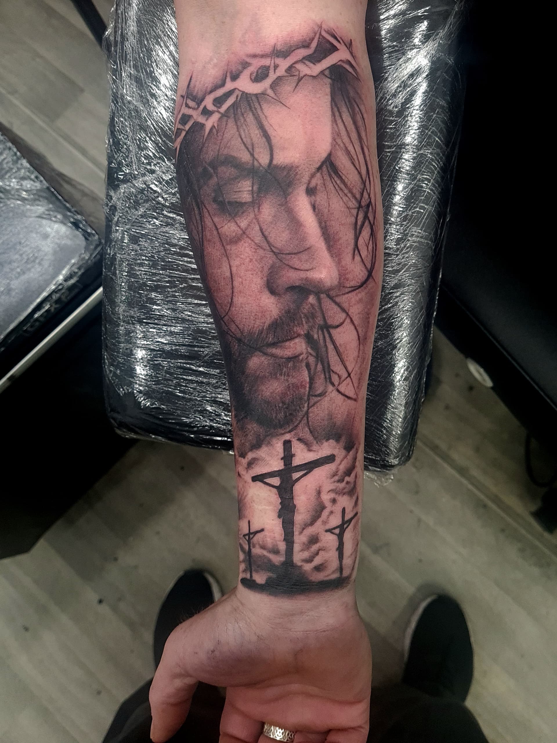 Realistic black and grey tattoo of Jesus with a crown of thorns on forearm.
