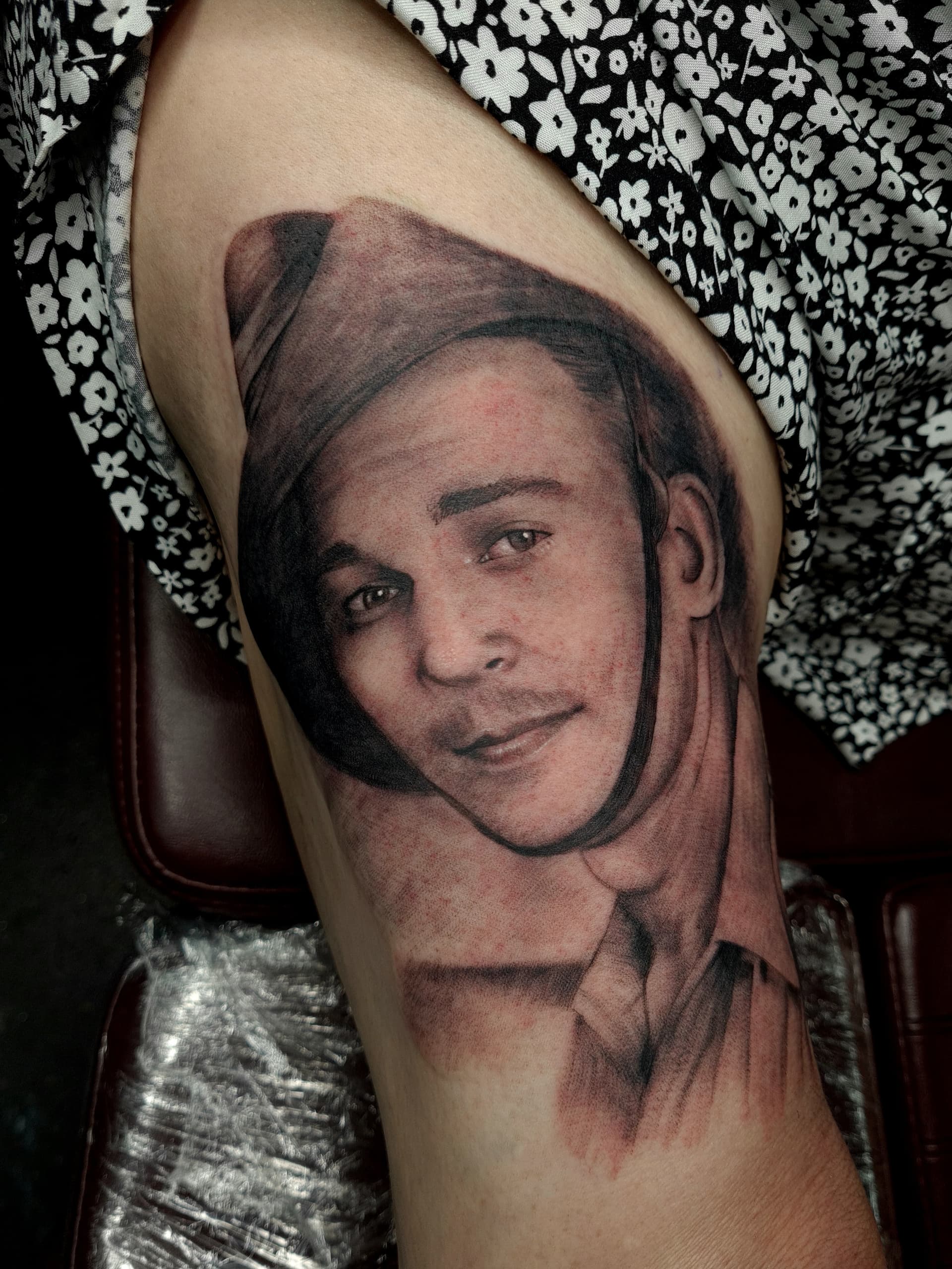 Black and grey realism tattoo of a man wearing a hat on thigh.