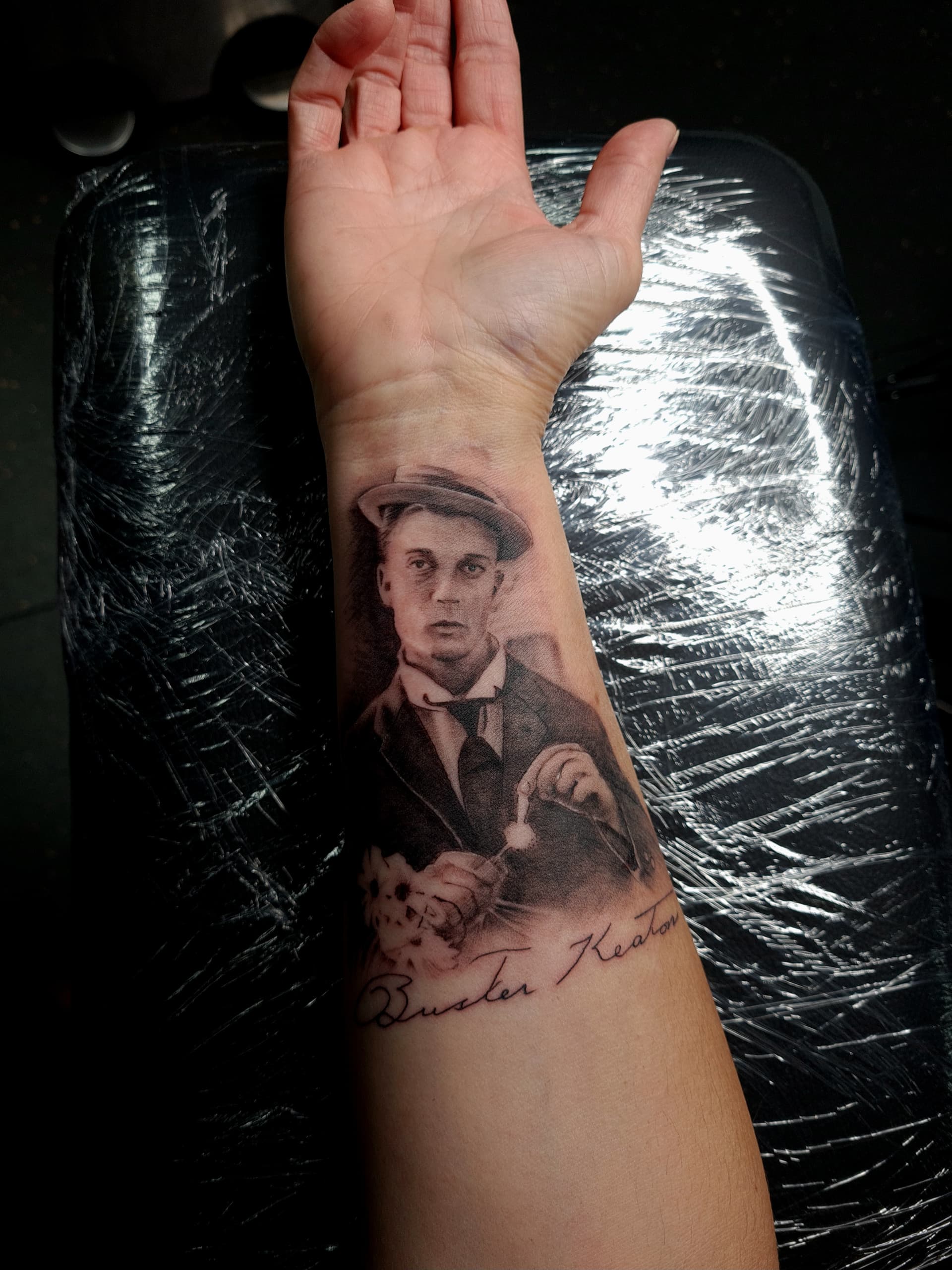 Realistic portrait tattoo of Buster Keaton on a person's forearm in black and grey.