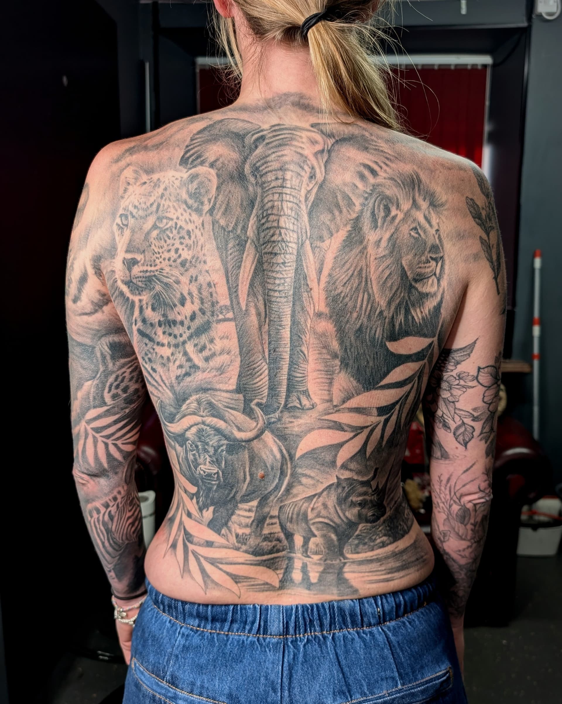 Black and grey realism tattoo of African wildlife including a lion, elephant, leopard and buffalo covering the back