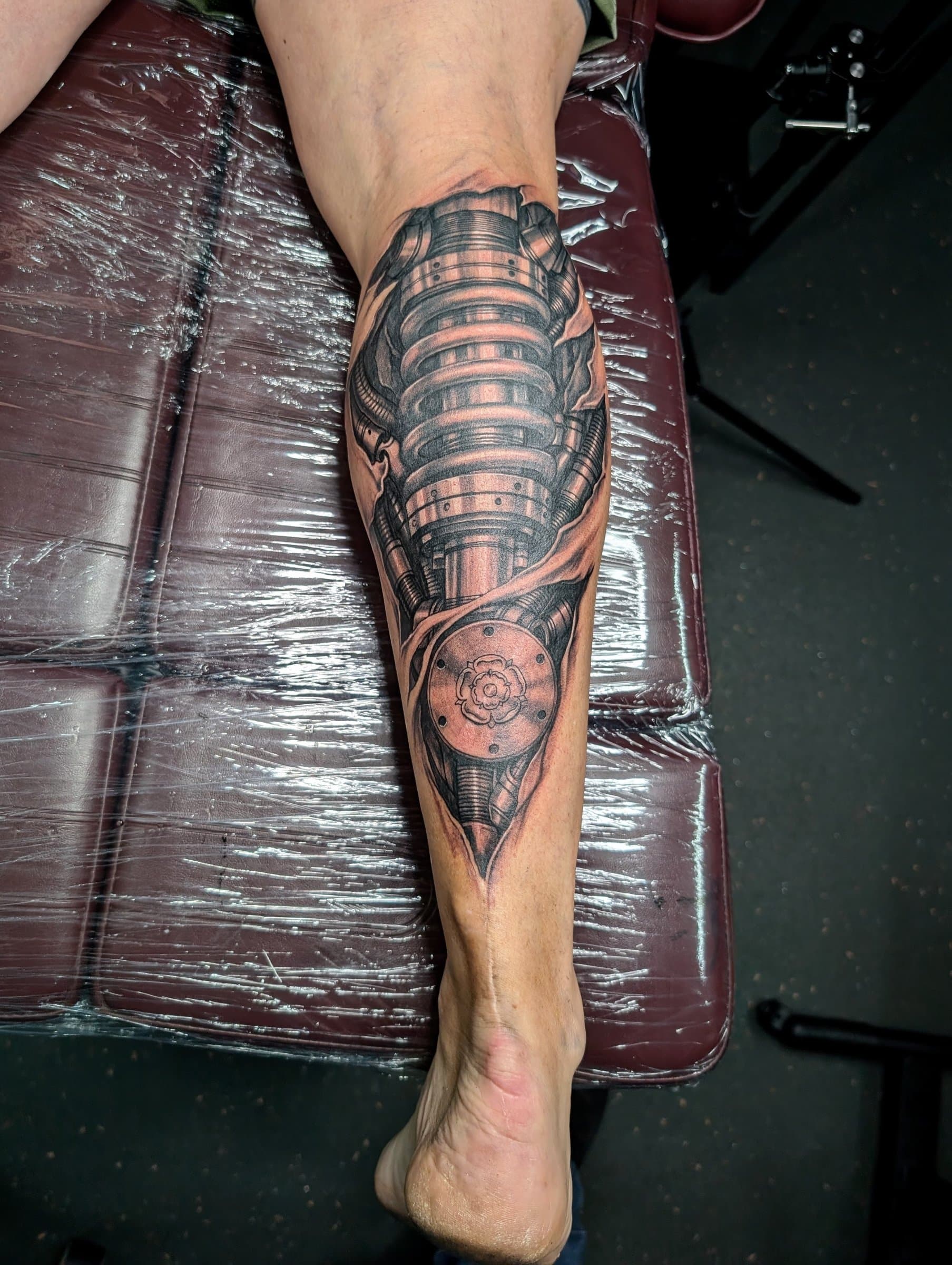 Black and grey realism biomechanical tattoo with a Yorkshire rose on the lower leg