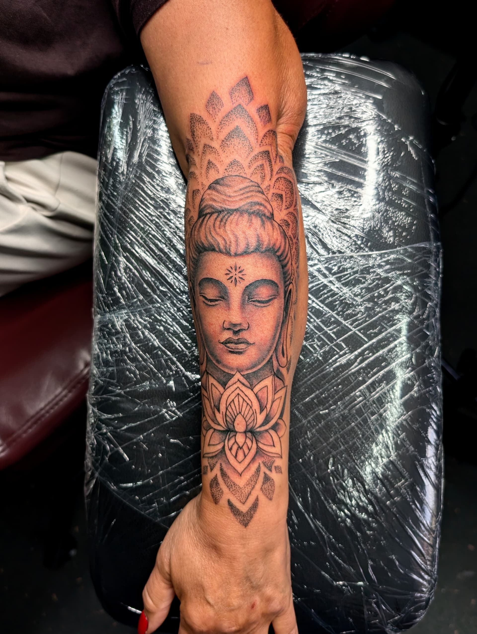 Black and grey realism tattoo of a Buddha face with a lotus flower on the forearm