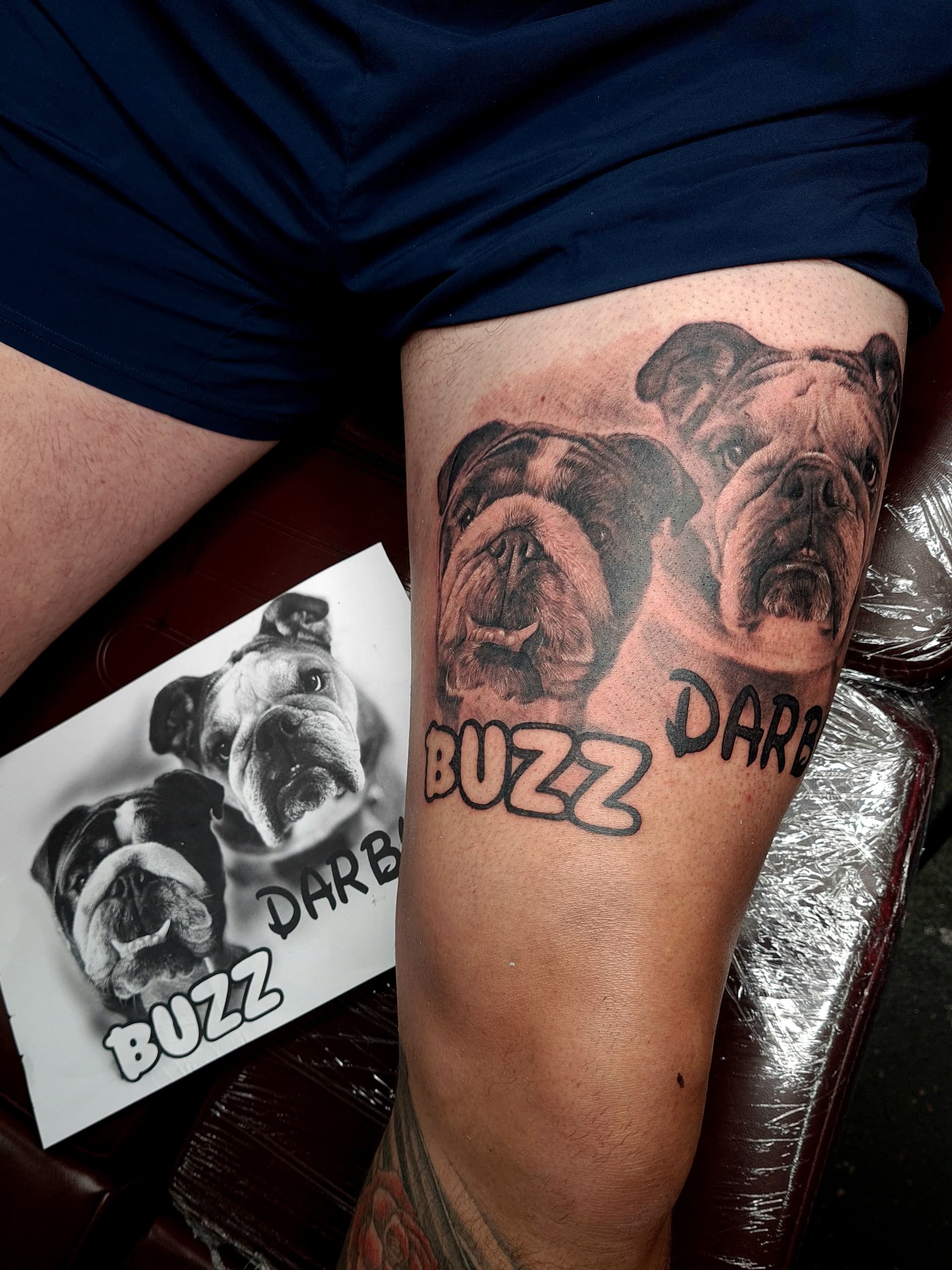 Black and grey realism tattoo of two bulldog pet portraits with names on the thigh
