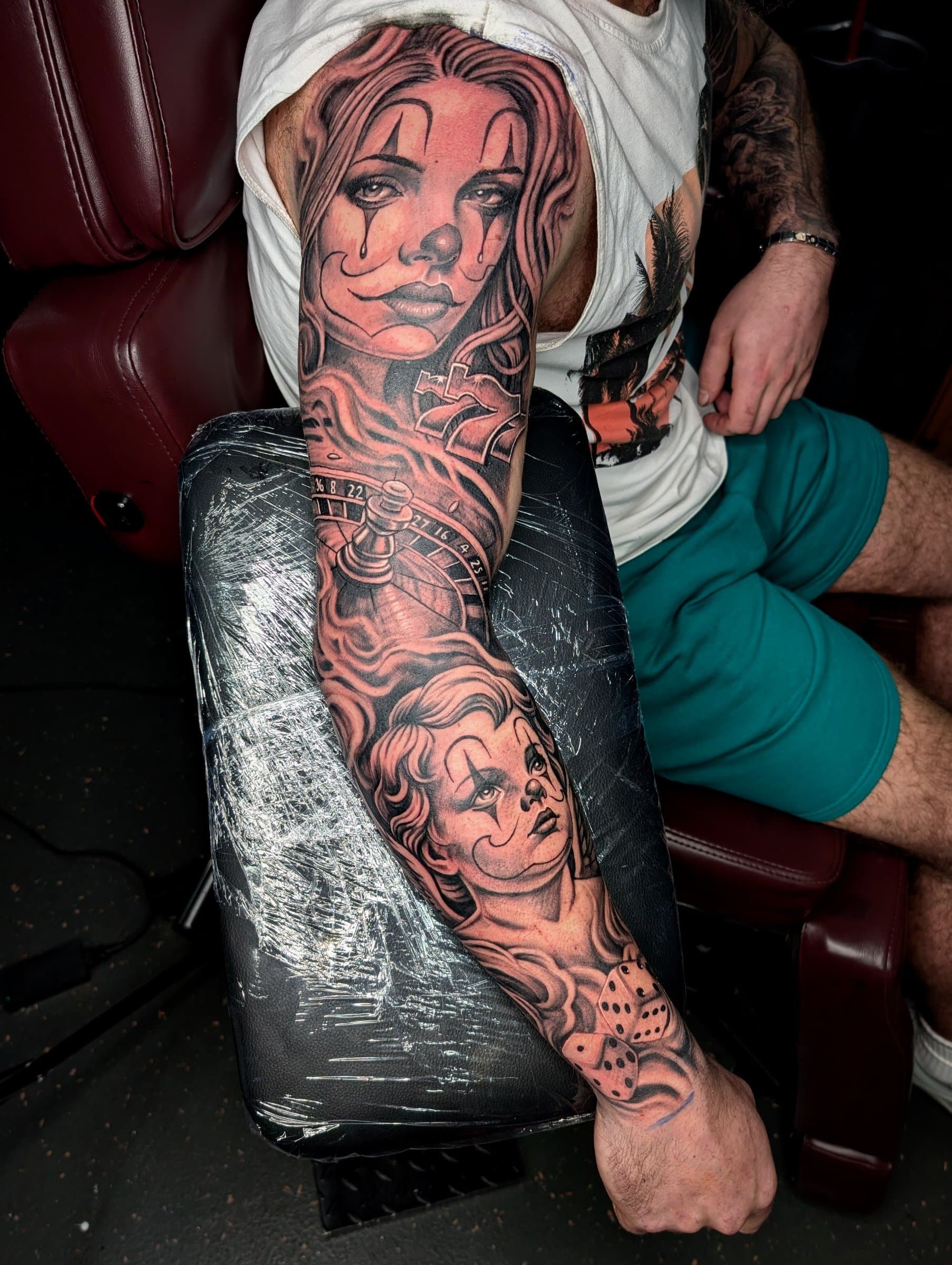 Black and grey realism arm sleeve tattoo of women in clown face paint with roulette wheel and dice