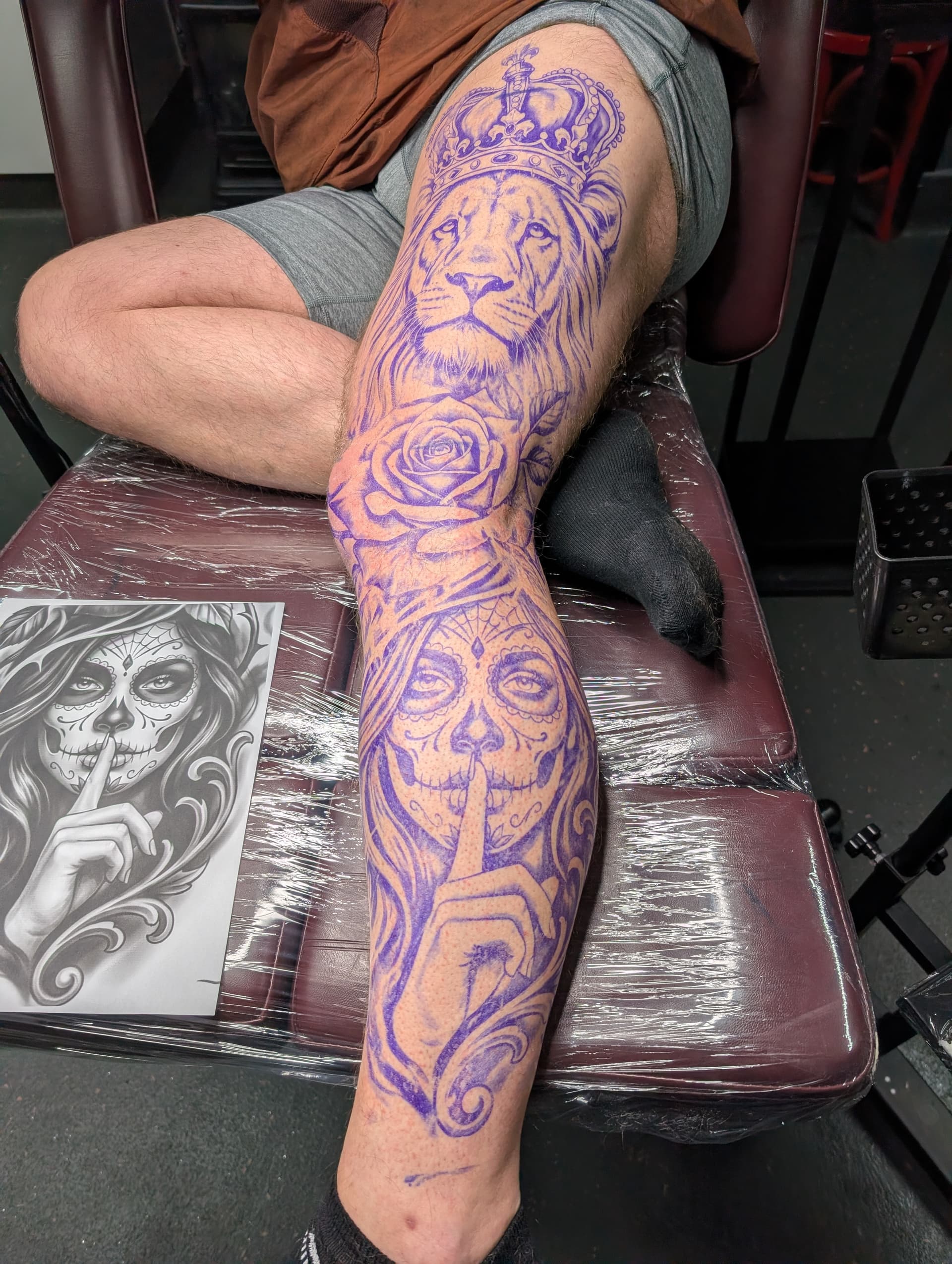Black and grey realism leg tattoo featuring a crowned lion, a rose and a sugar skull woman's face