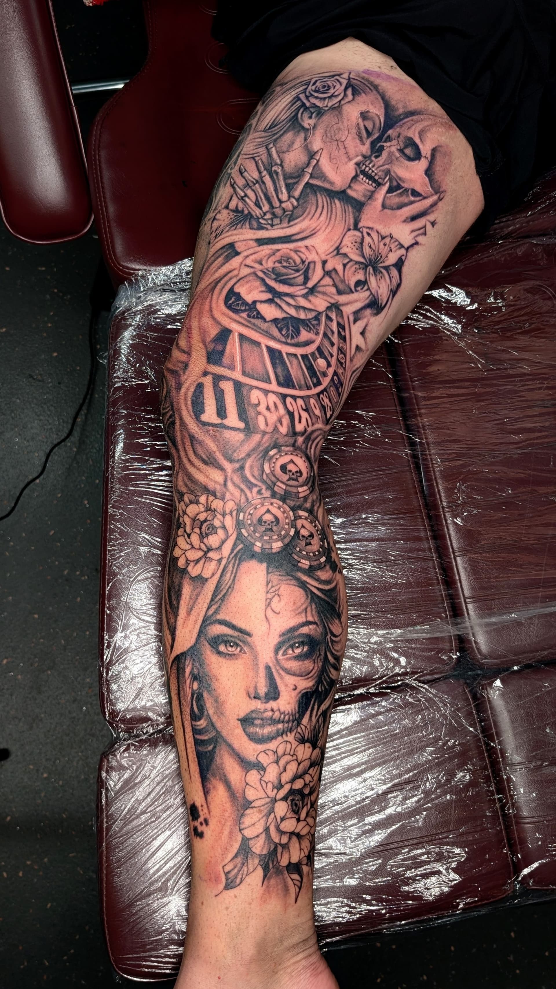 Black and grey realism leg sleeve tattoo featuring skull face paint women, a skull, roulette wheel and roses