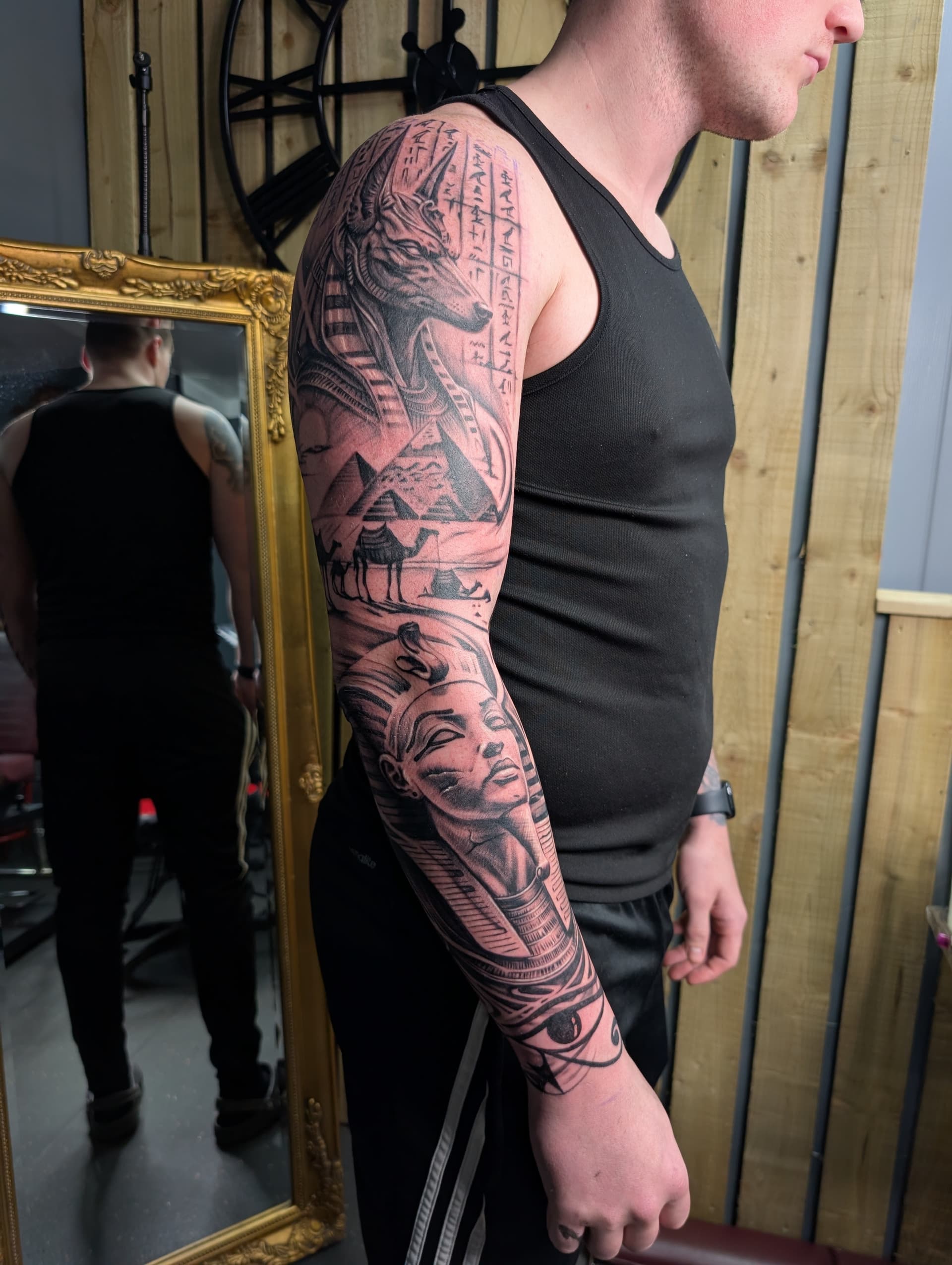Black and grey realism arm sleeve tattoo featuring Anubis, pyramids and a pharaoh's face