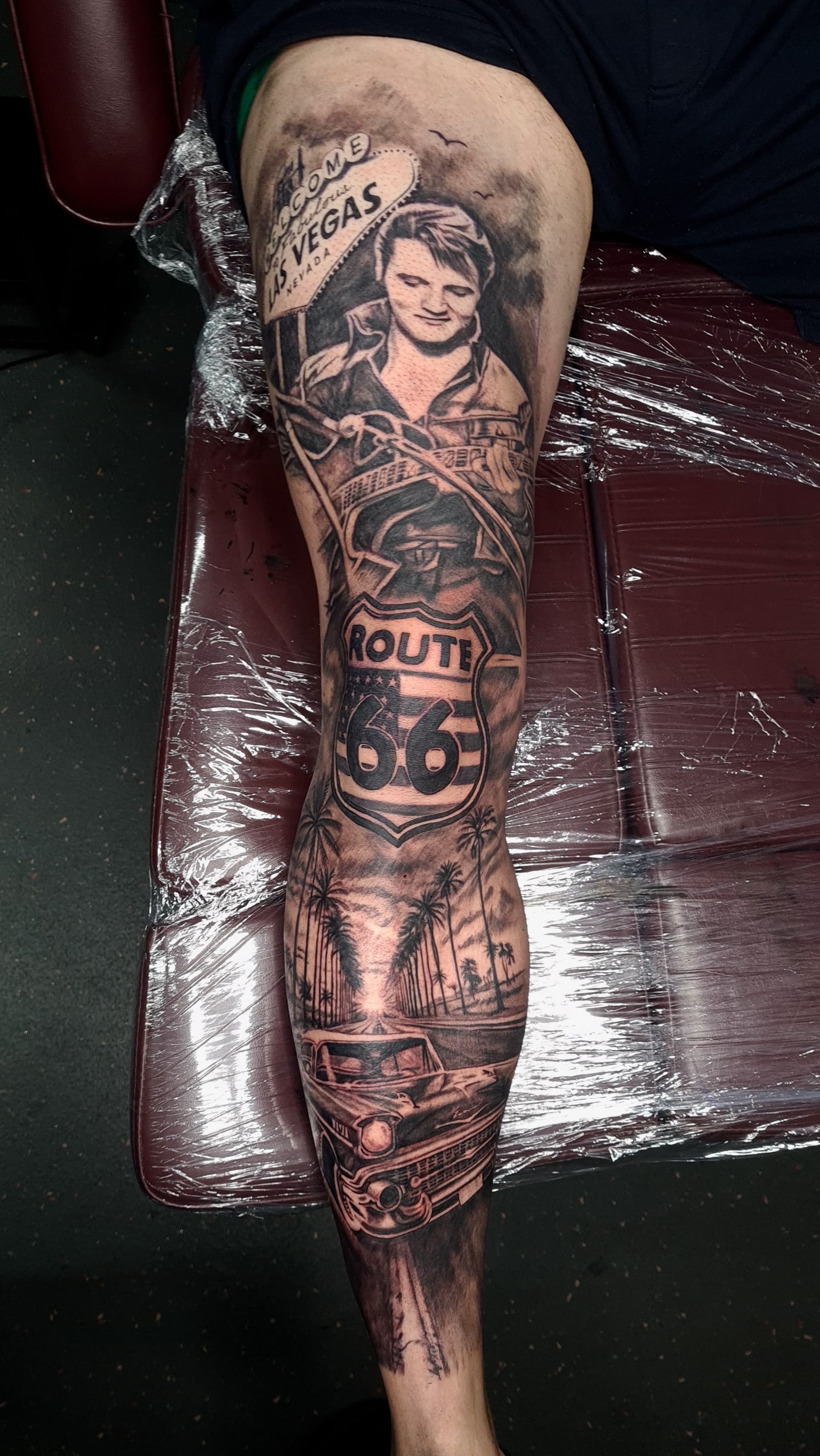 Black and grey realism leg sleeve tattoo featuring an Elvis portrait, Las Vegas sign, Route 66 shield and palm trees
