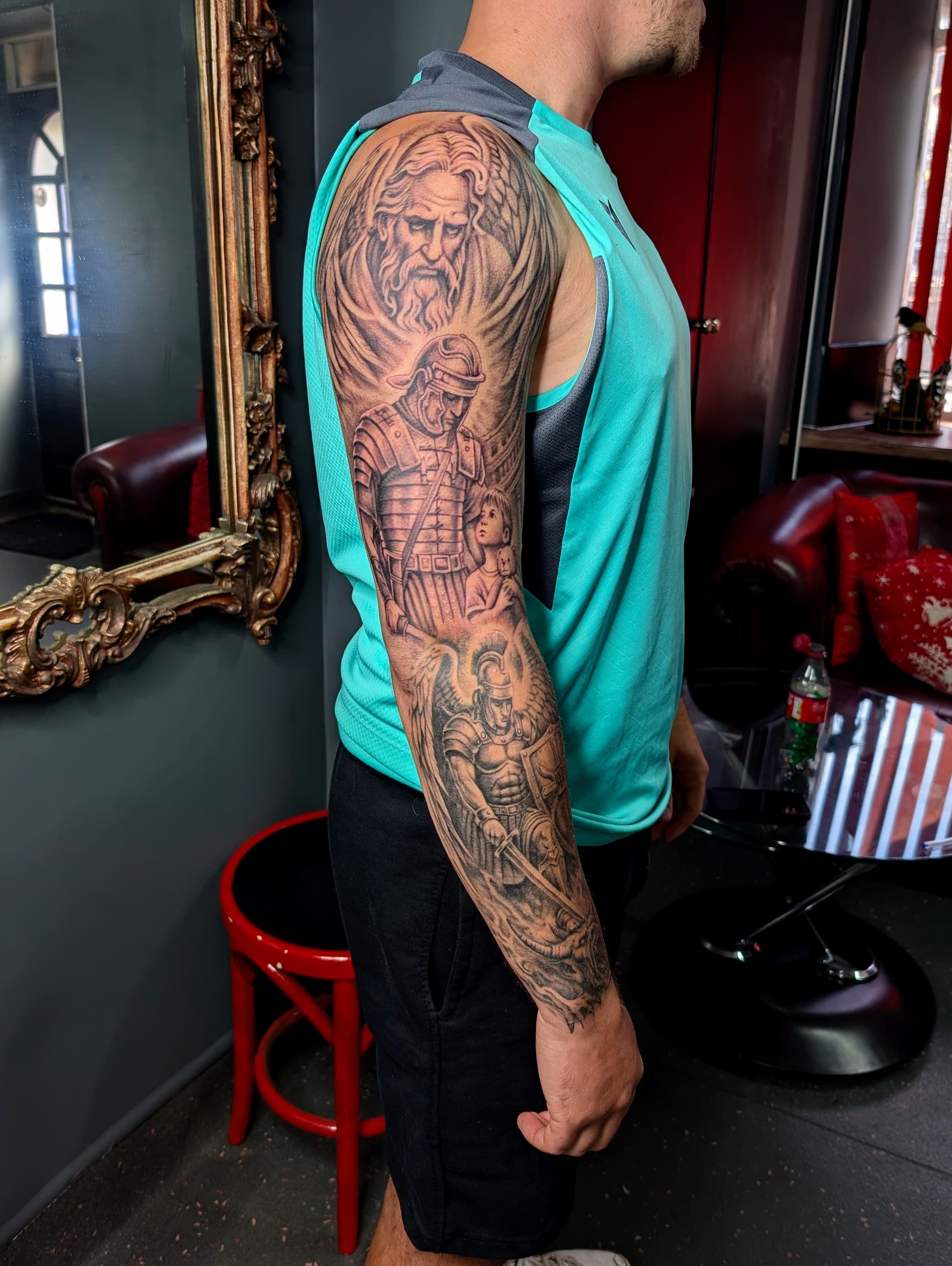 Black and grey realism arm sleeve tattoo featuring a winged angel, Roman soldiers and a child