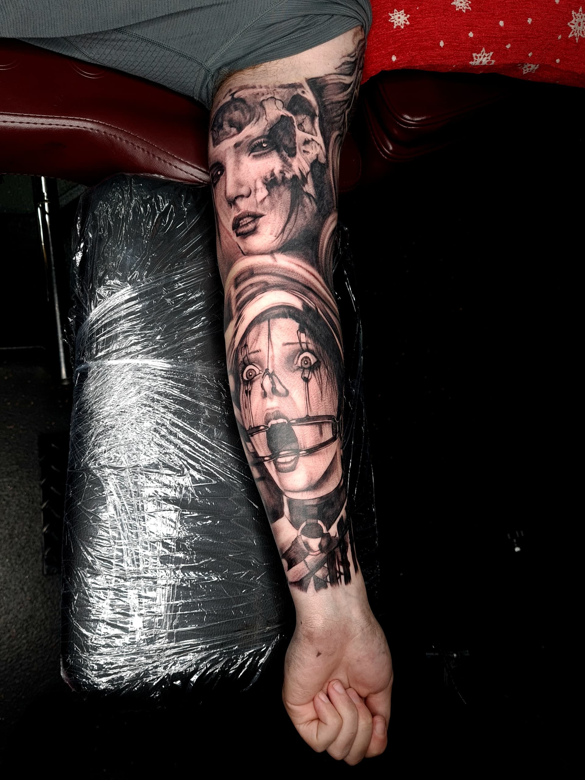 Black and grey realism tattoo of a skull-faced woman and a restrained screaming figure on the forearm