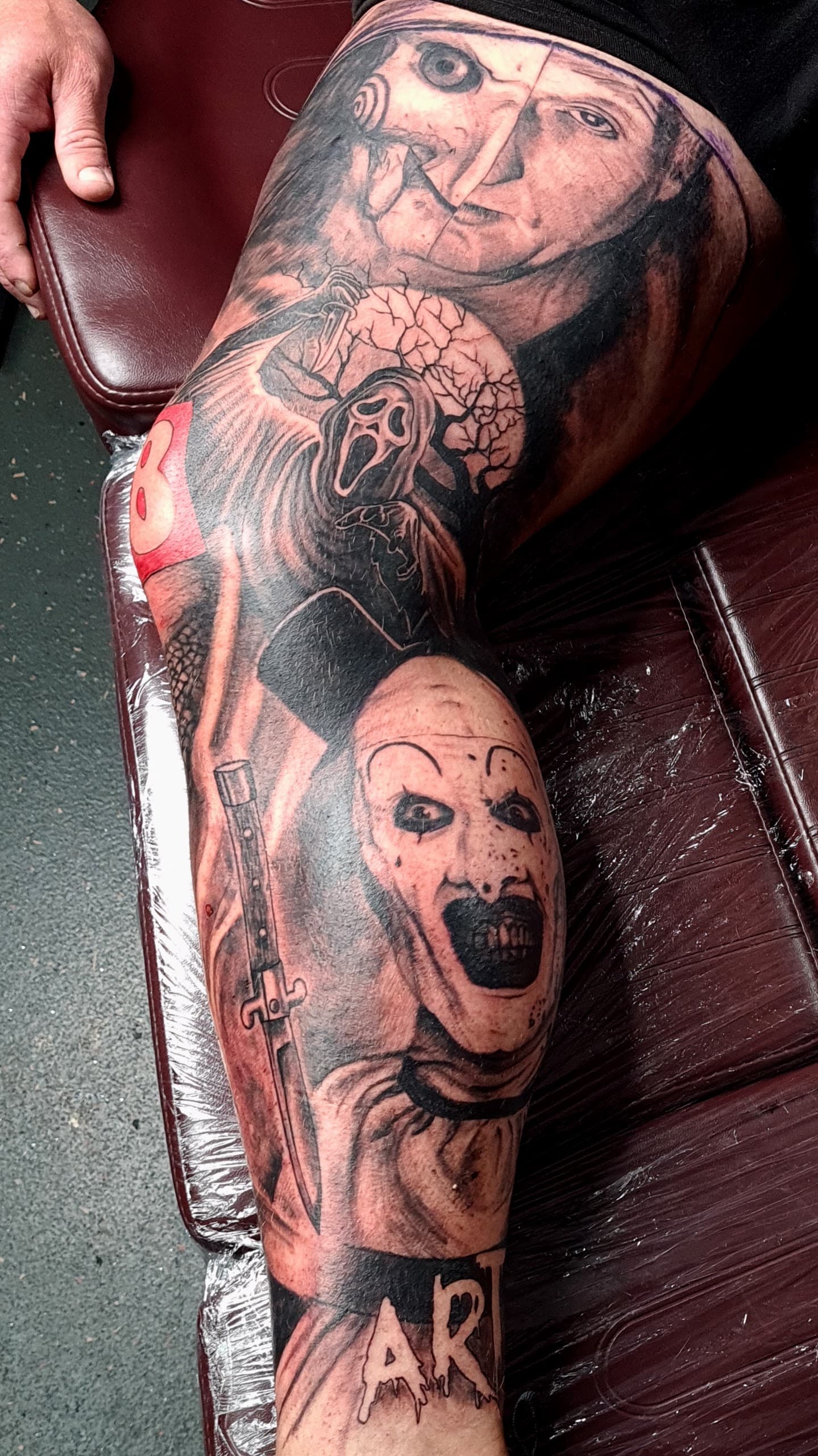 Black and grey realism tattoo of horror movie characters including a puppet and ghost mask on the thigh