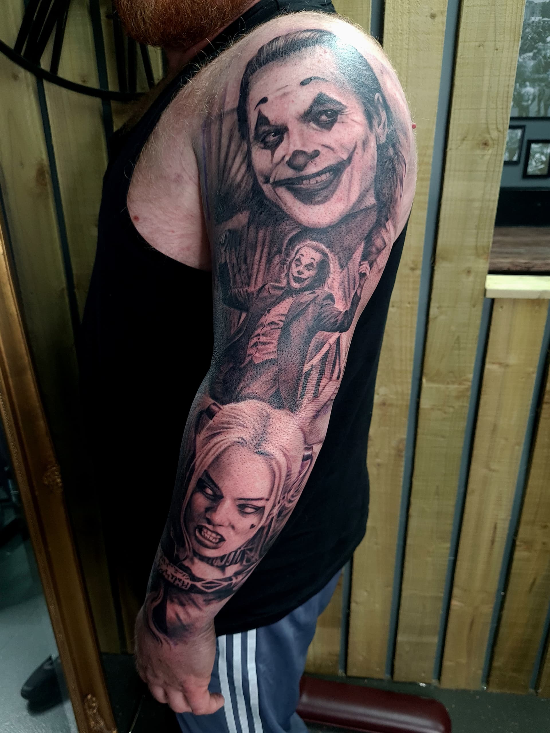 Black and grey realism arm sleeve tattoo featuring the Joker and Harley Quinn characters