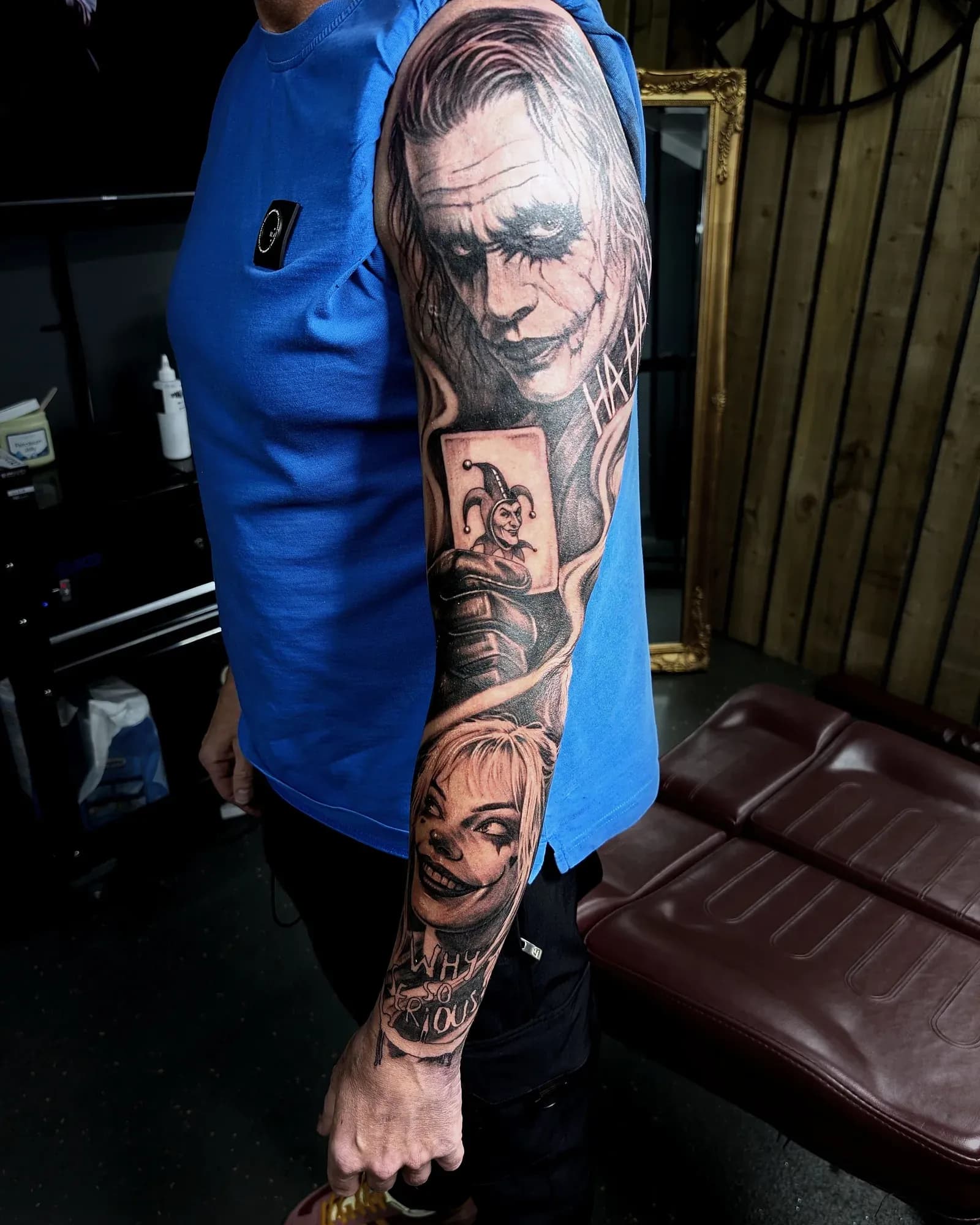 Black and grey realism tattoo of Joker and Harley Quinn themed cover-up of an old tribal, with 'Why so serious' lettering on