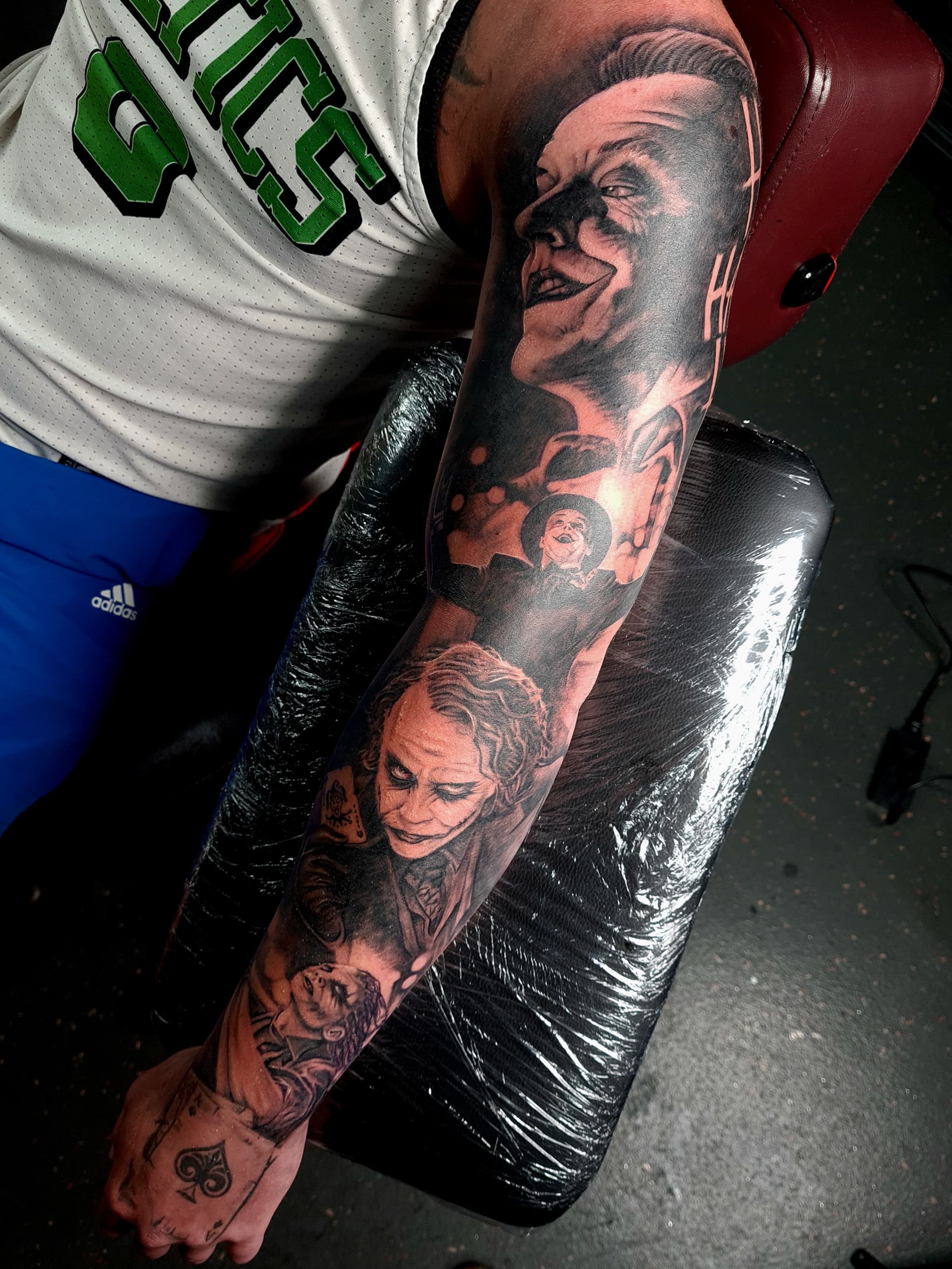 Black and grey realism tattoo sleeve depicting multiple versions of the Joker character down the arm
