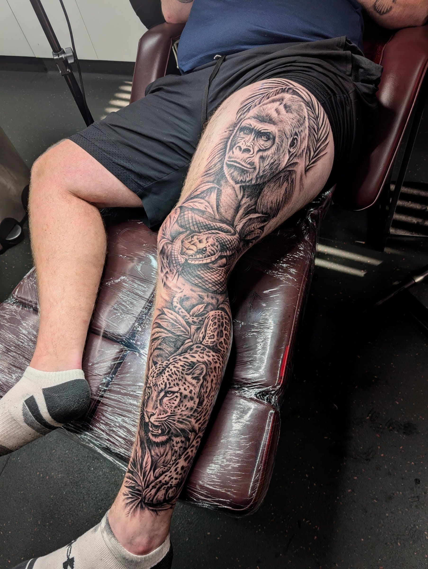 Black and grey realism leg sleeve tattoo featuring a gorilla, snake and leopard in jungle foliage