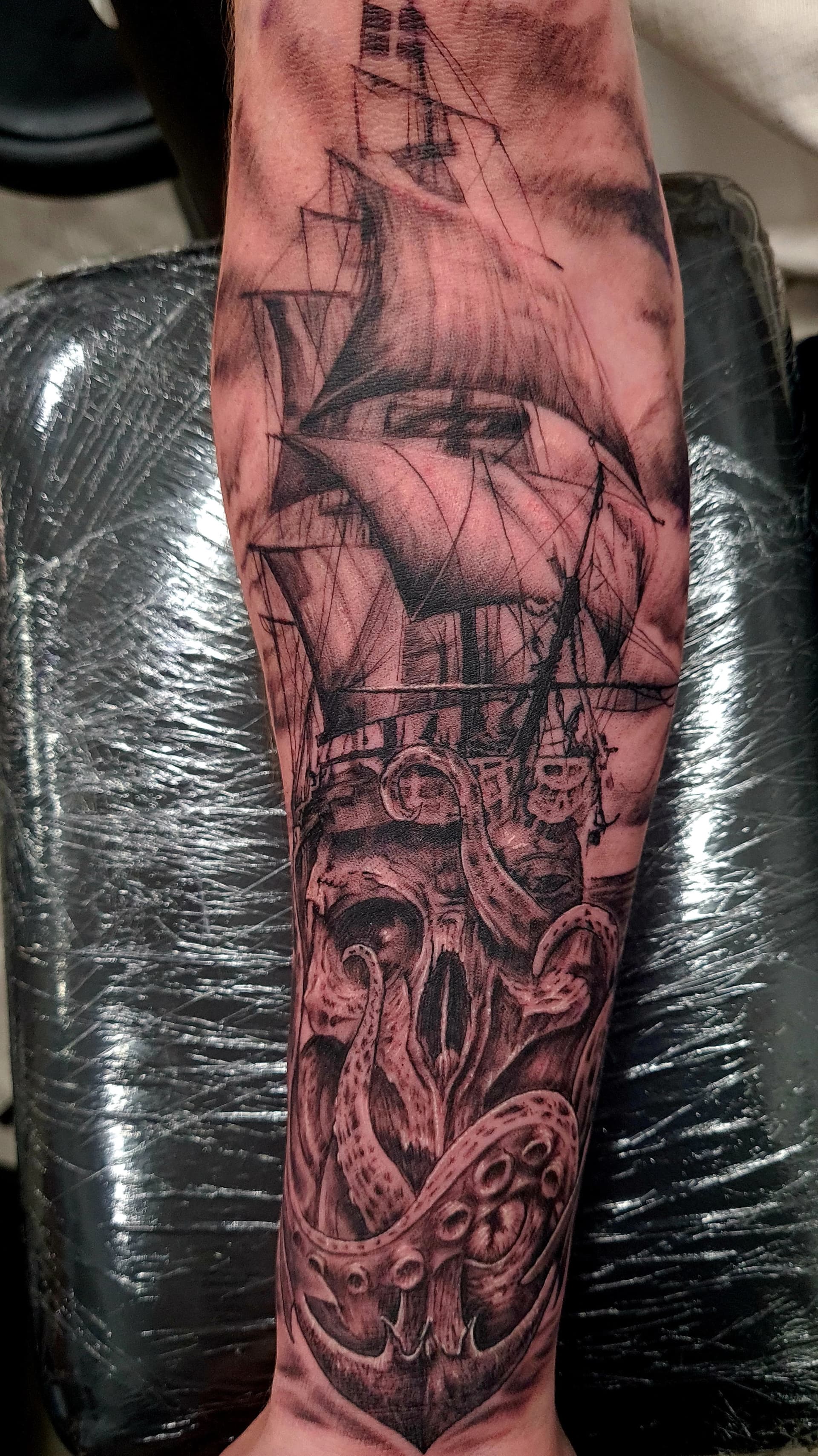 Black and grey realism tattoo of a kraken's tentacles wrapped around a sailing ship on the forearm