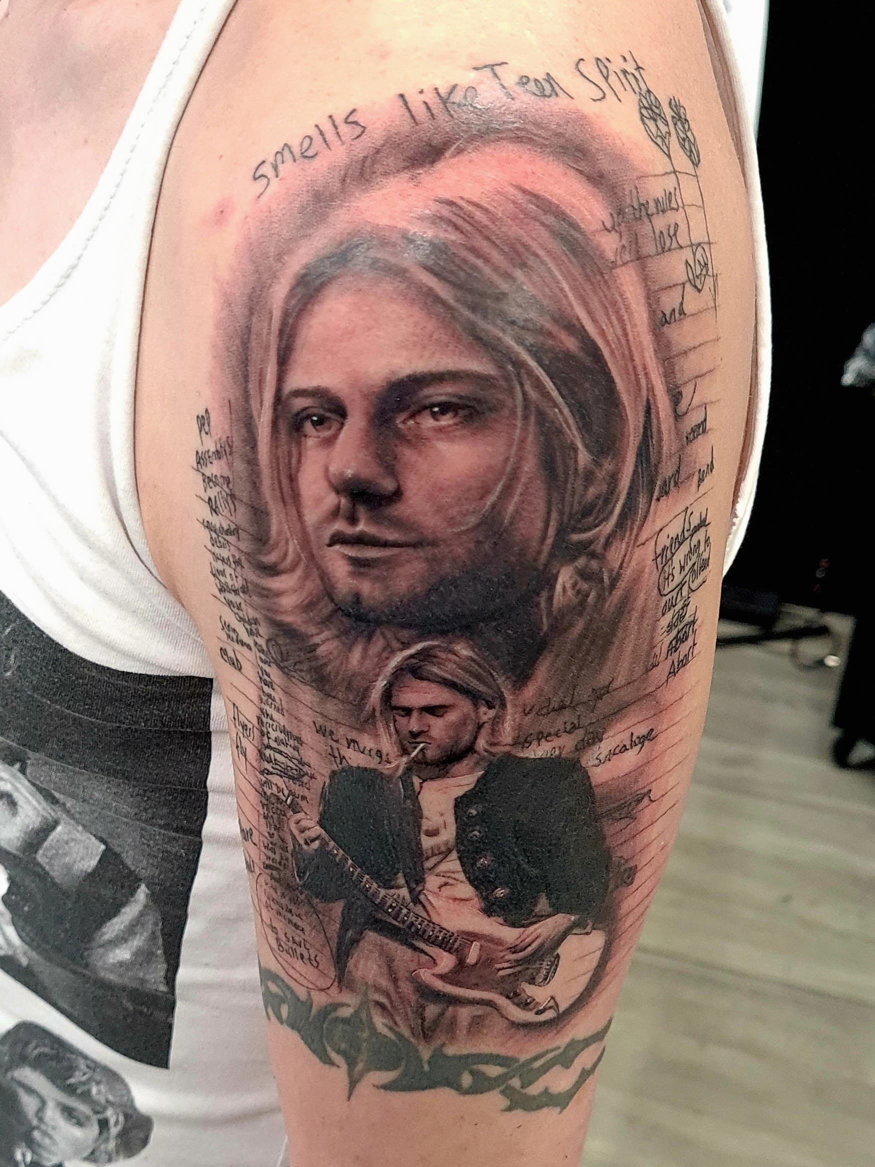 Black and grey realism tattoo of Kurt Cobain's portrait with handwritten lyrics on the upper arm