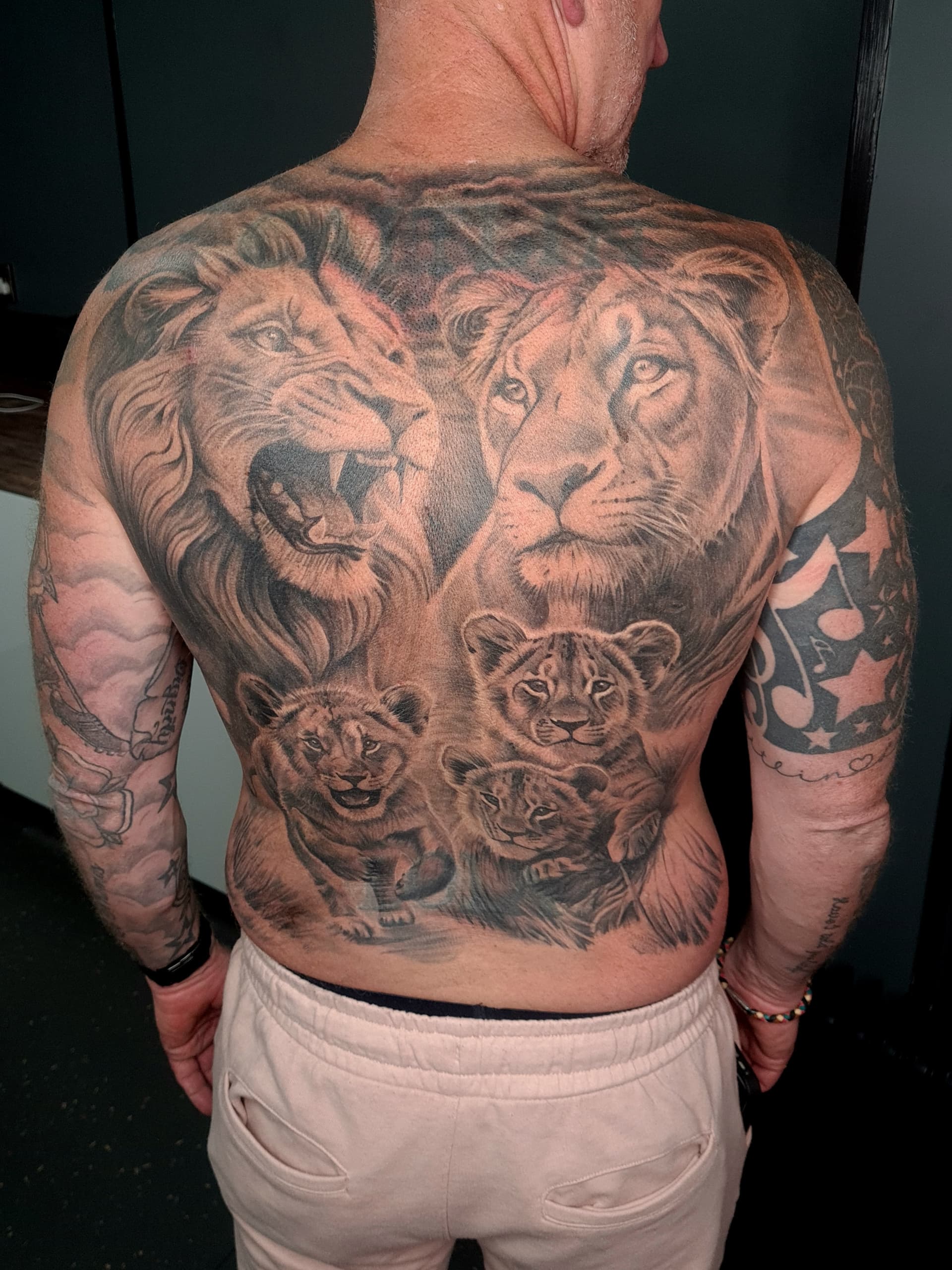 Black and grey realism tattoo of a lion, lioness and cubs covering the back