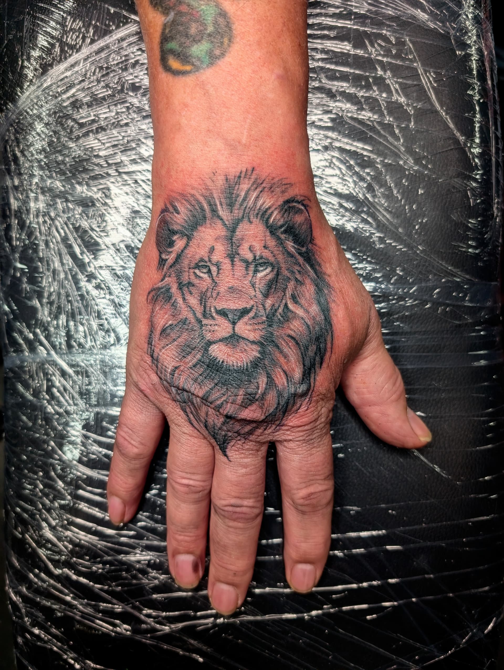 Black and grey realism tattoo of a lion's face on the back of the hand