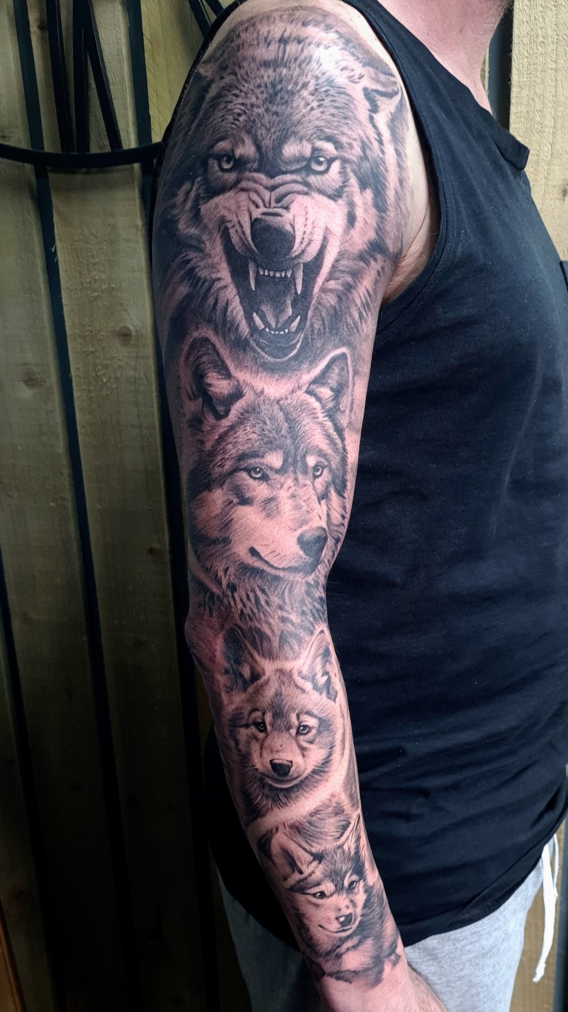 Black and grey realism tattoo of several wolf faces covering the full arm