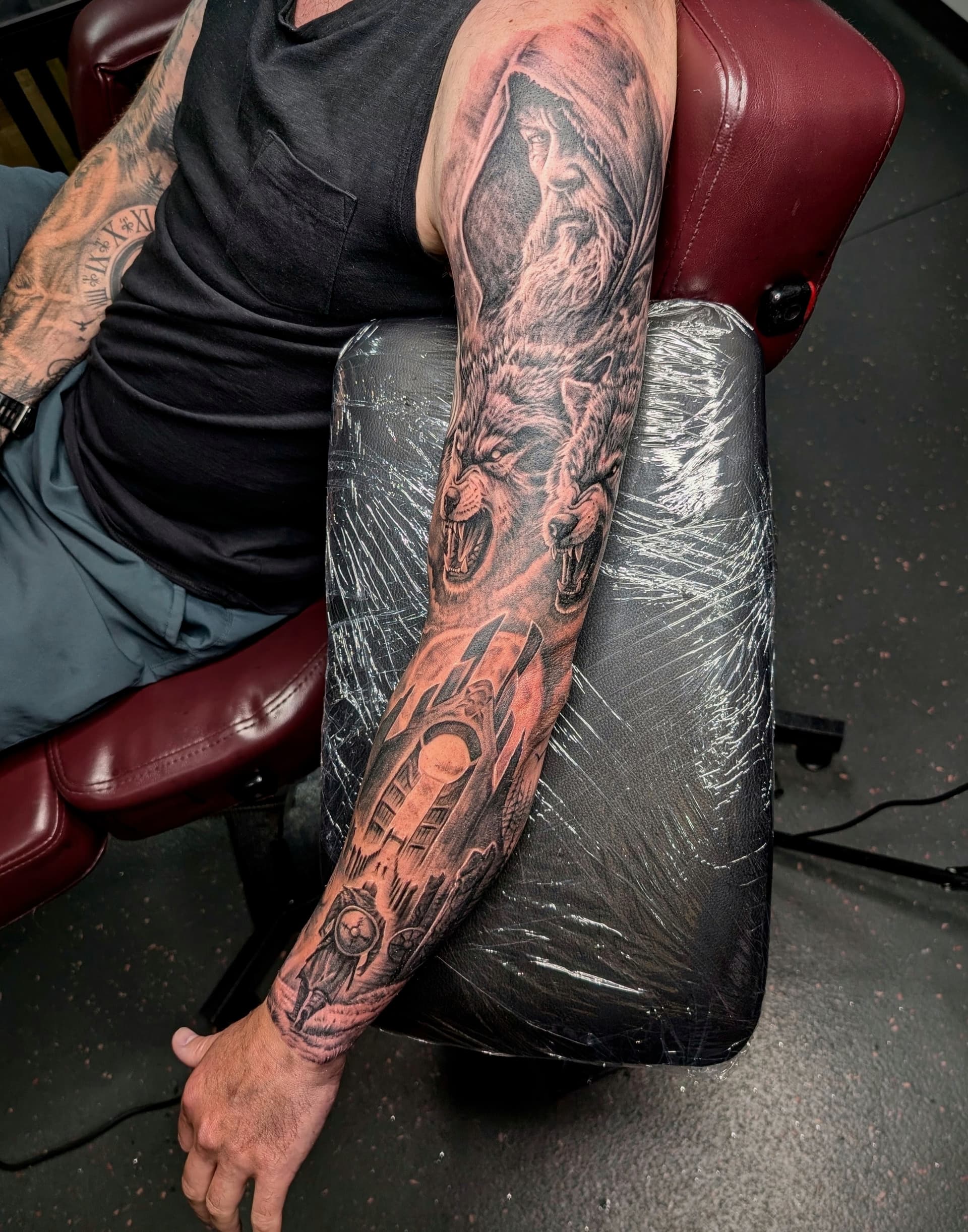 Black and grey realism tattoo sleeve of a hooded wizard, snarling wolves and a Viking longship on the full arm