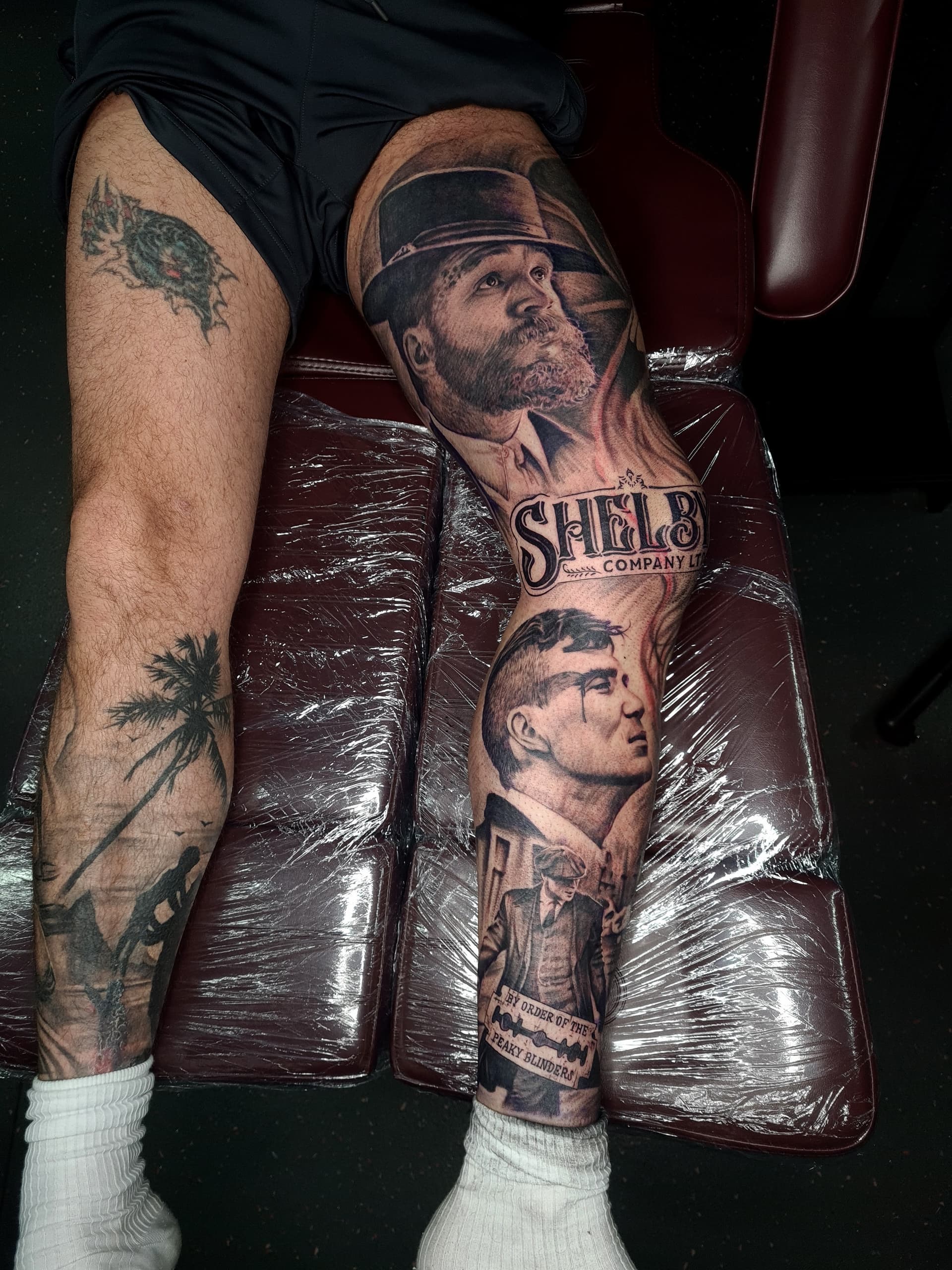 Black and grey realism leg sleeve tattoo depicting Peaky Blinders characters and Shelby Company Ltd lettering