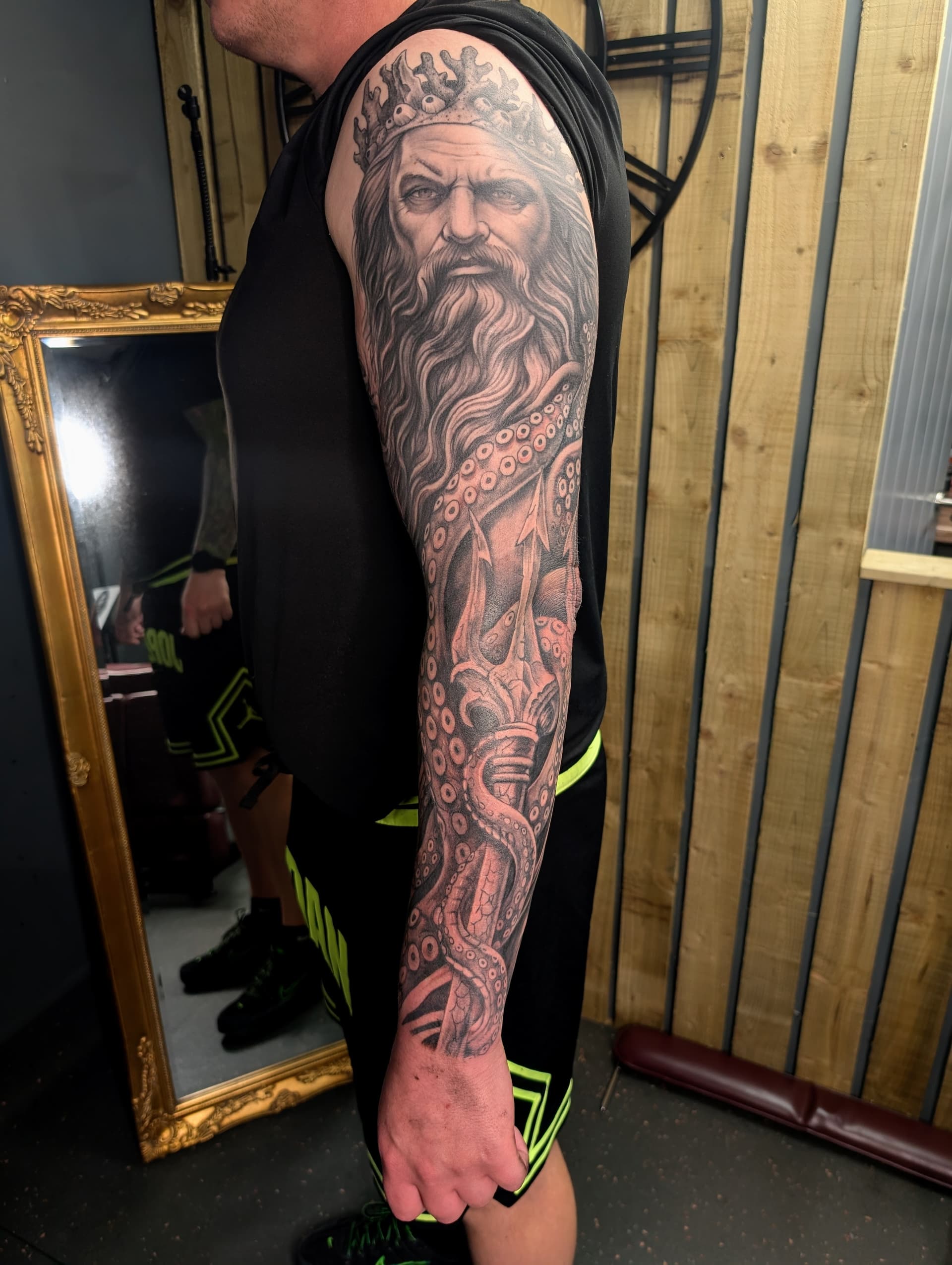 Black and grey realism tattoo of Poseidon with crown, trident and octopus tentacles covering the full arm