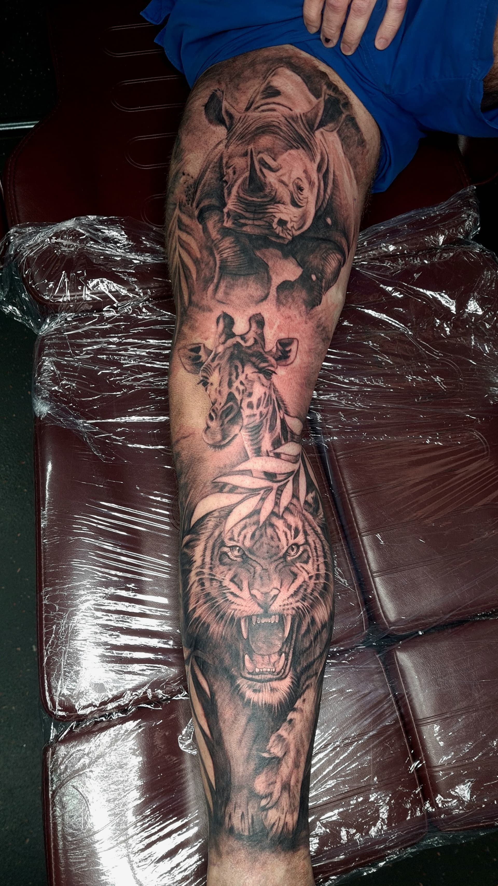 Black and grey realism tattoo of a rhino, giraffe and roaring tiger on the thigh