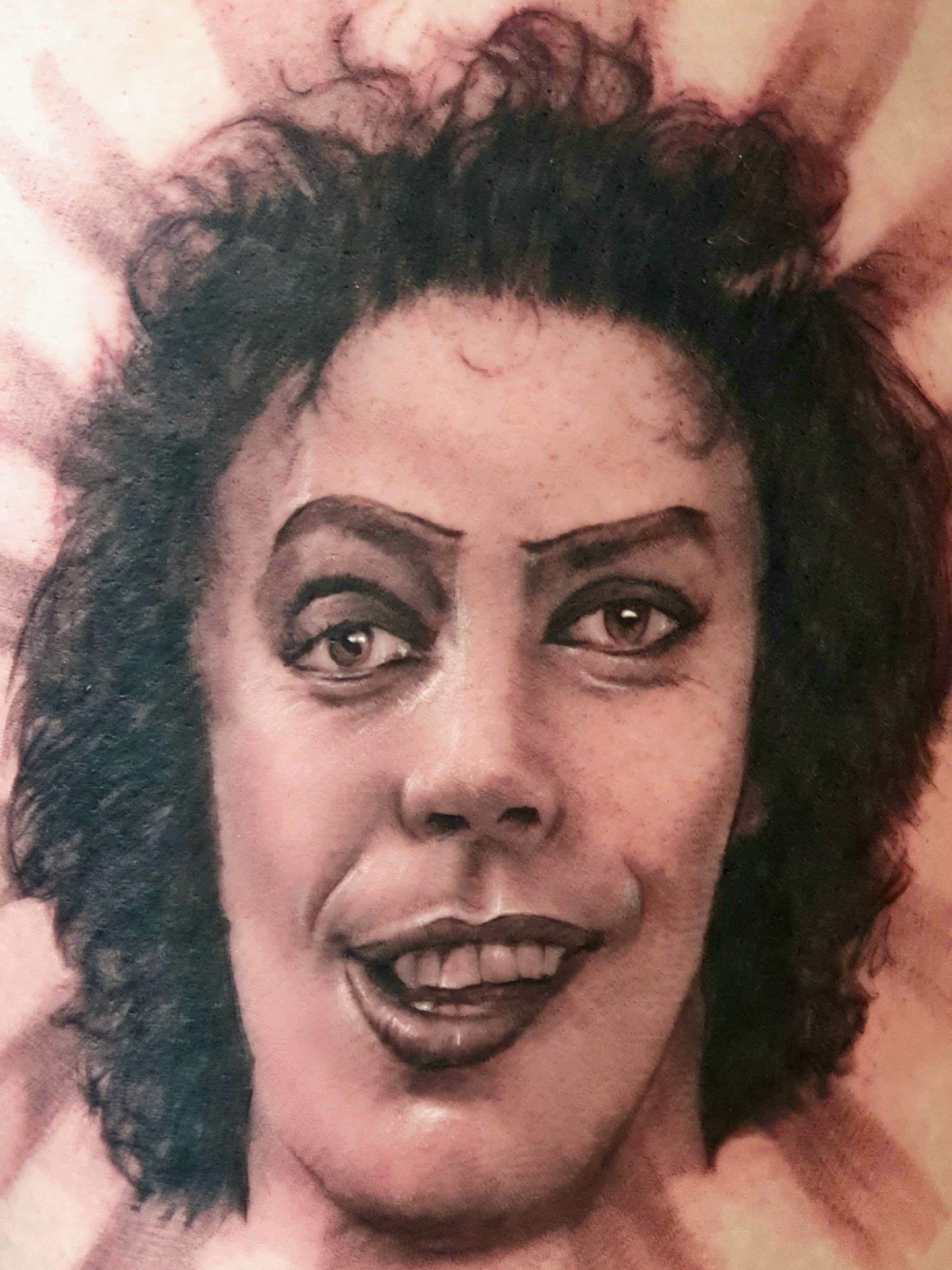 Black and grey realism tattoo of a smiling curly-haired film character's face