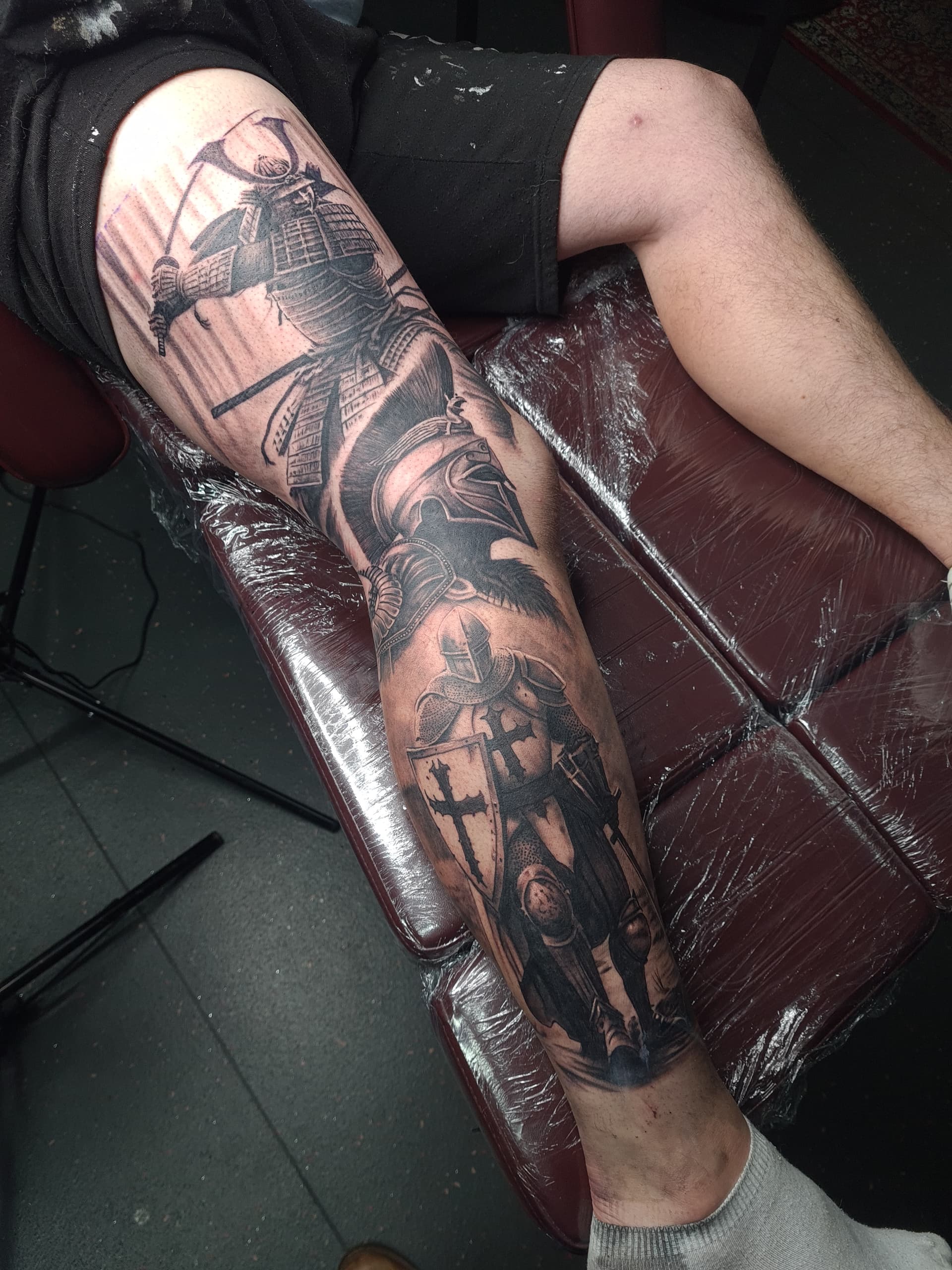 Black and grey realism leg sleeve tattoo featuring a samurai, Spartan helmet and Crusader knight warriors