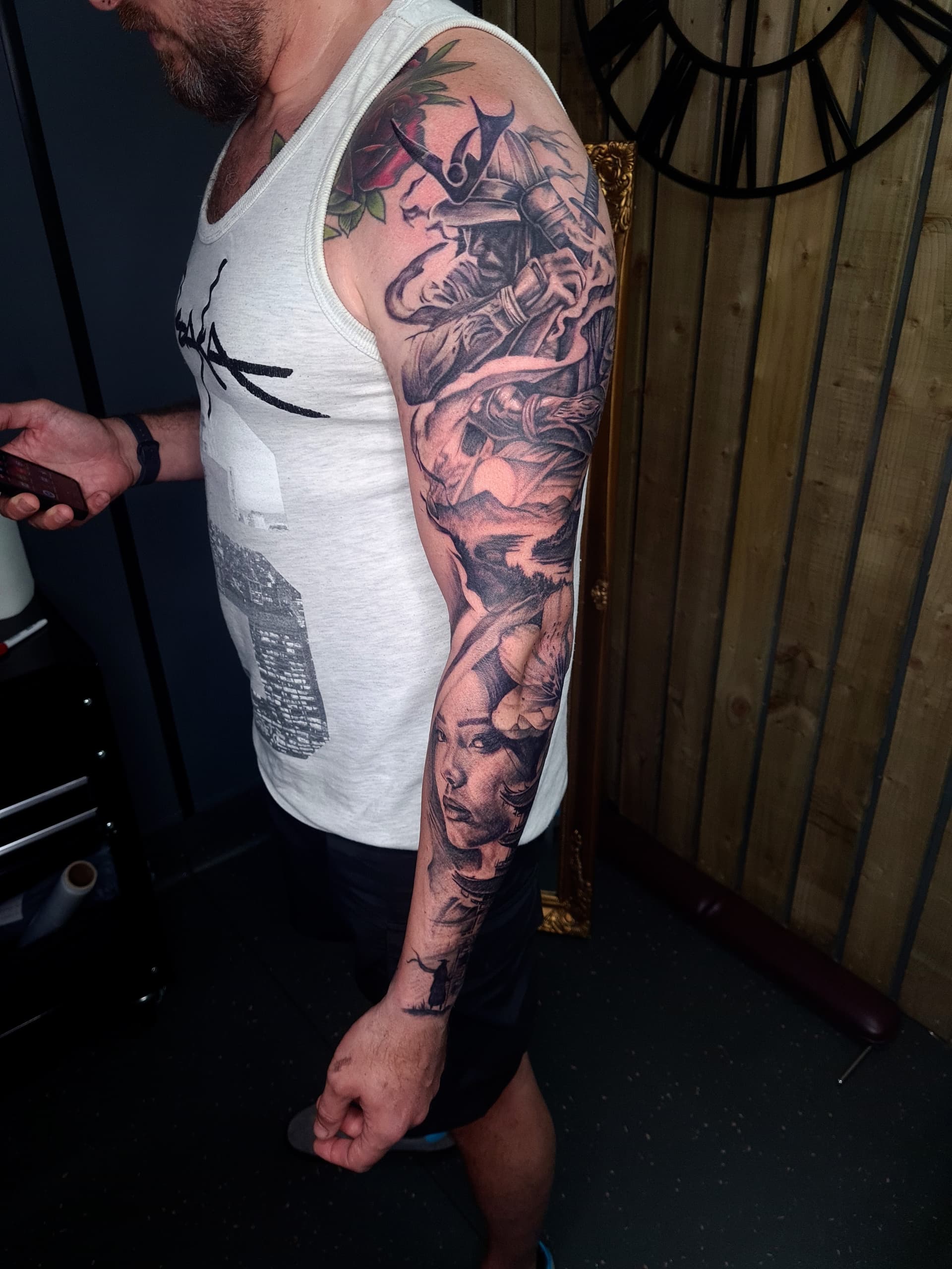 Black and grey realism arm sleeve tattoo of a horned samurai warrior, geisha portrait and mountain scenery