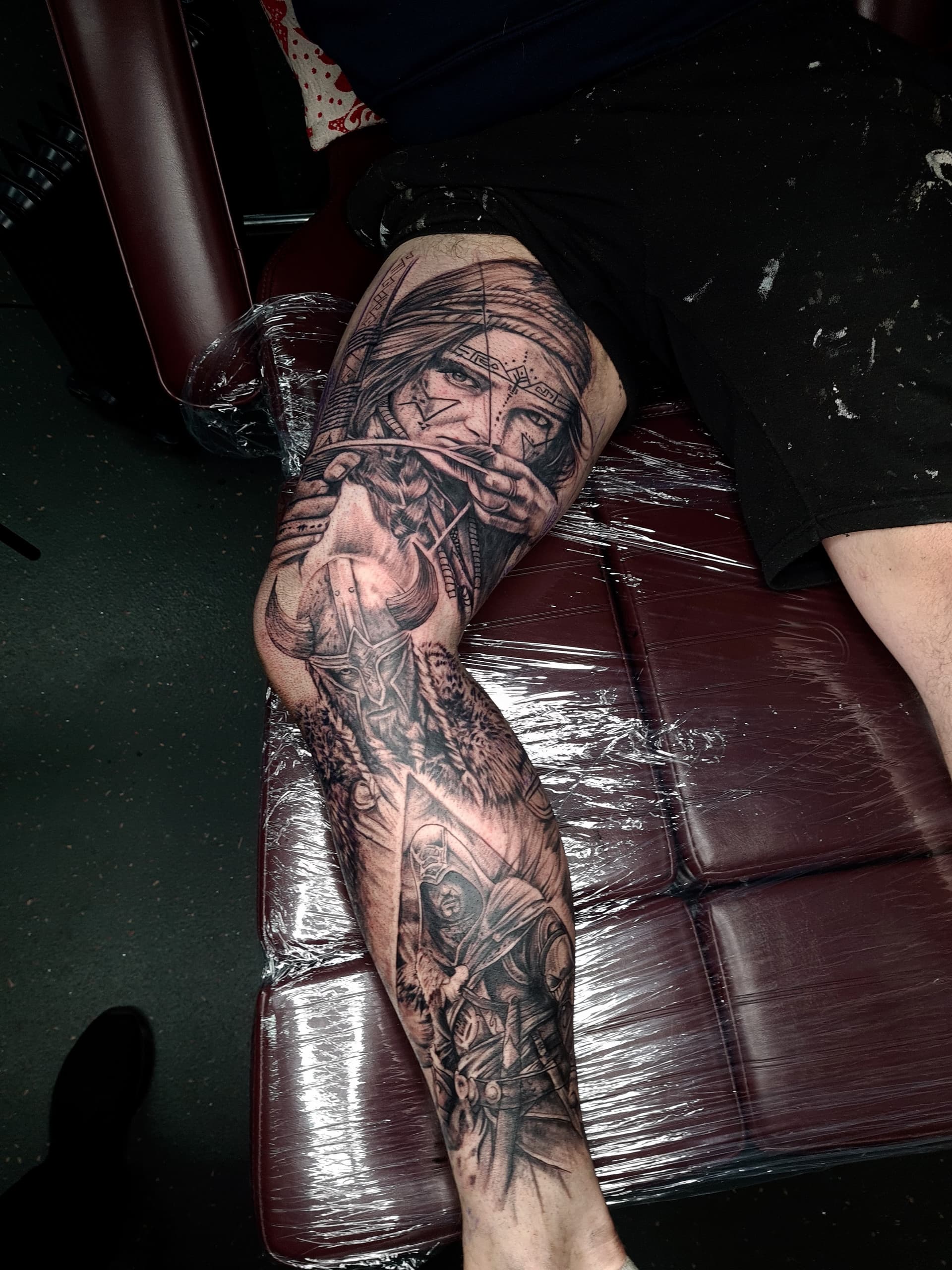 Black and grey realism leg sleeve tattoo of Viking warriors, an archer and a horned helmet