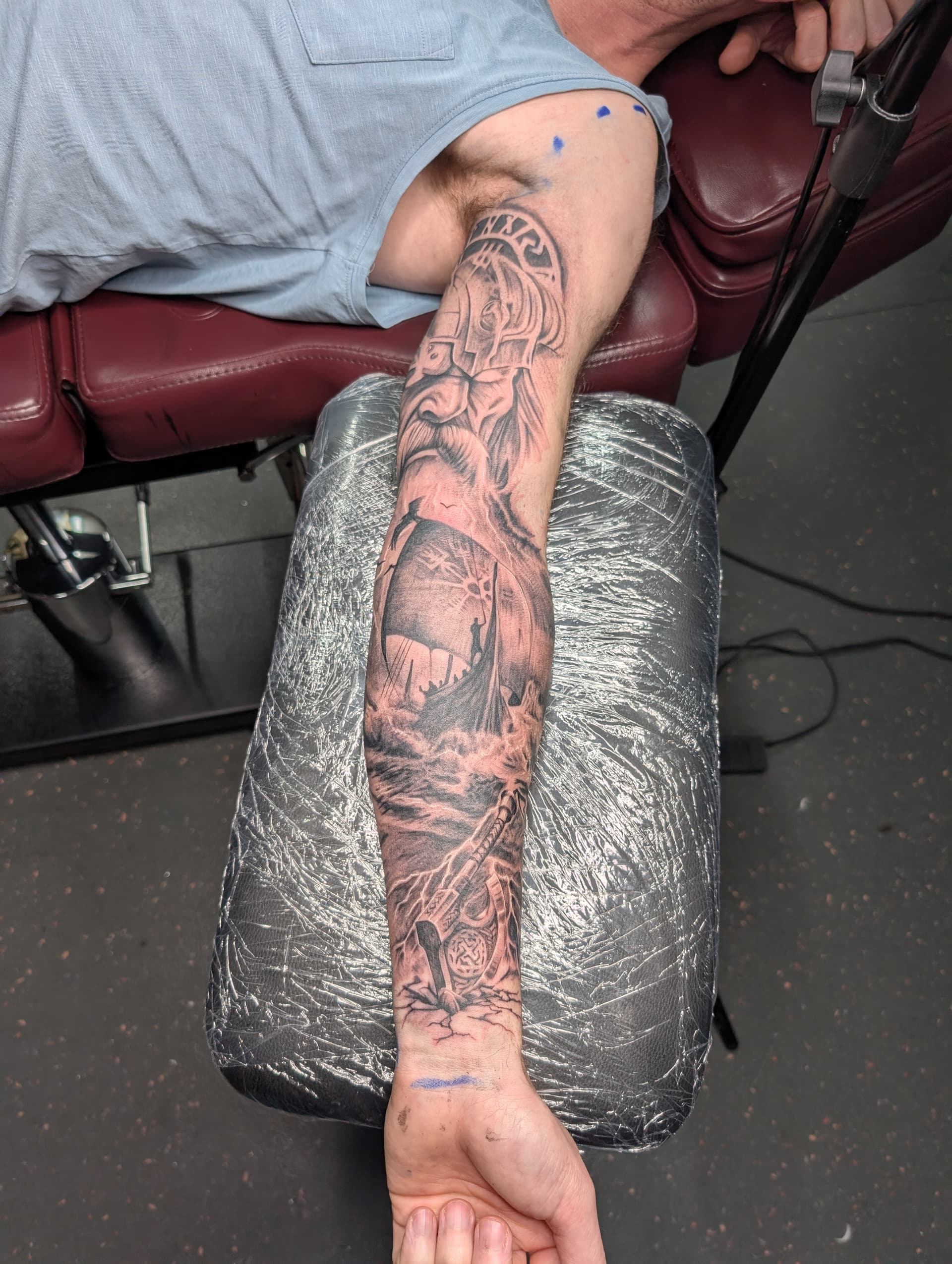 Black and grey realism tattoo of a Viking warrior, longship and axe on the forearm