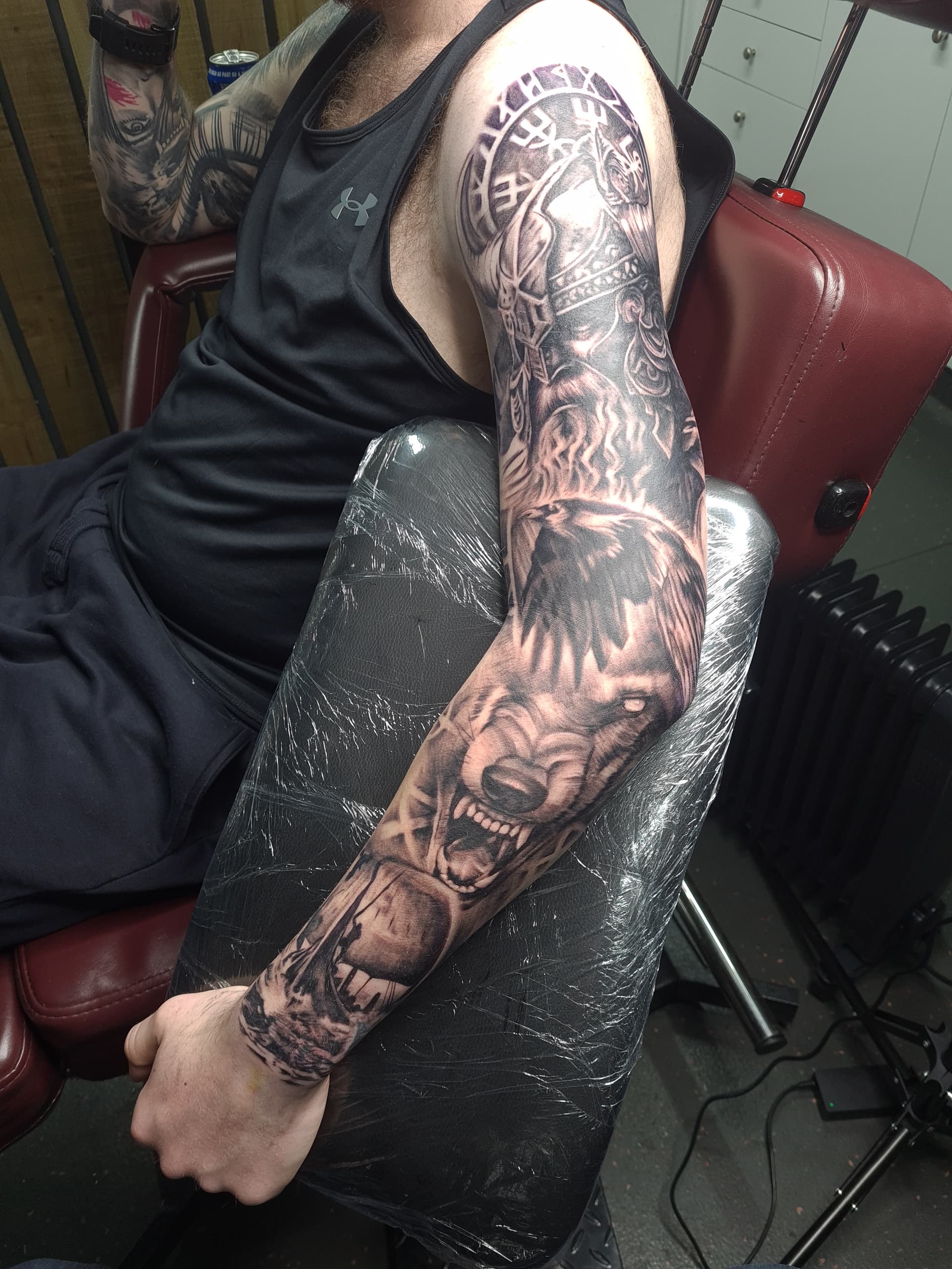 Black and grey realism tattoo sleeve of a Viking warrior, raven and snarling wolf covering the full arm