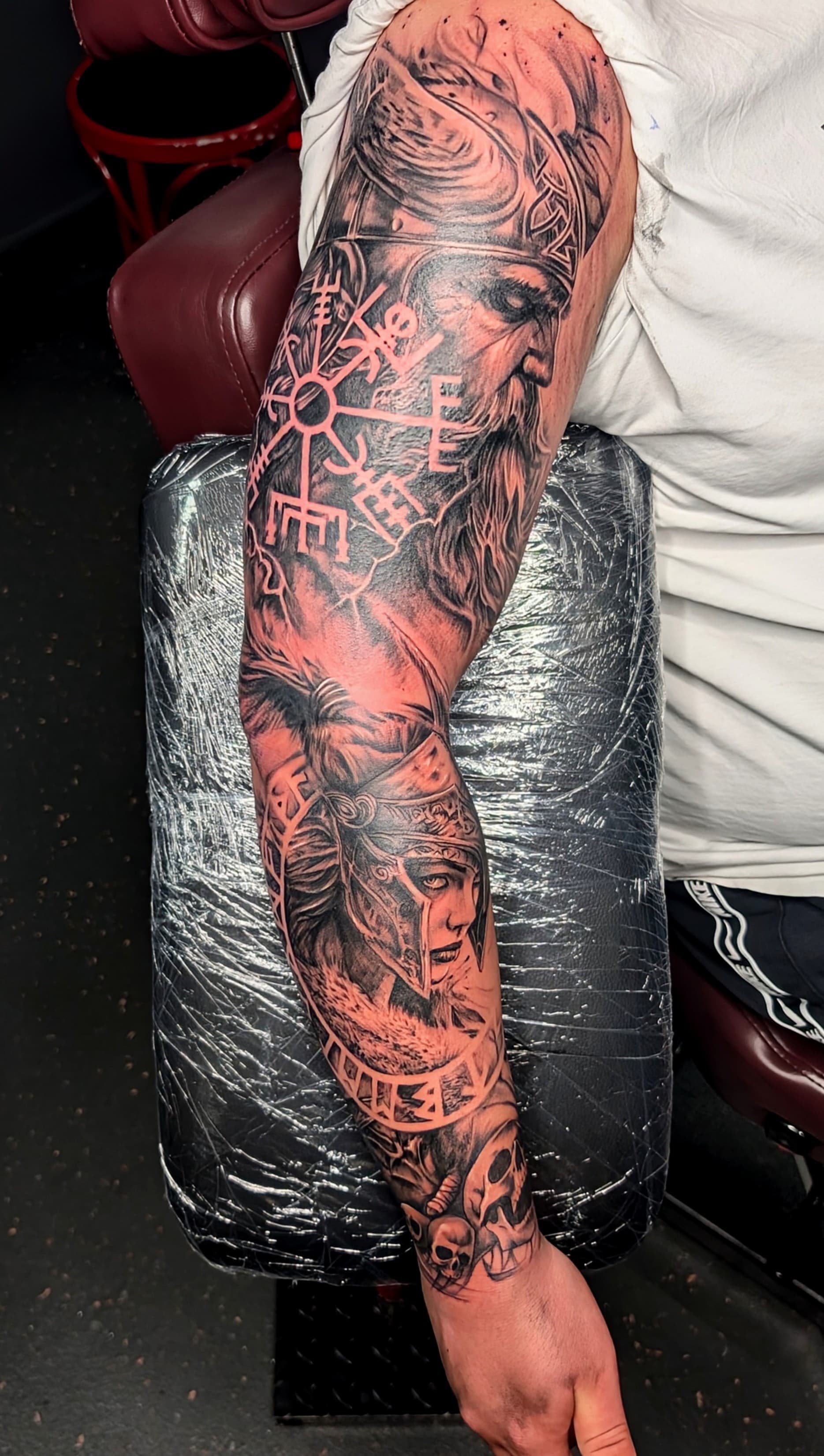 Black and grey realism tattoo sleeve of a Viking warrior, runic compass and skulls covering the full arm
