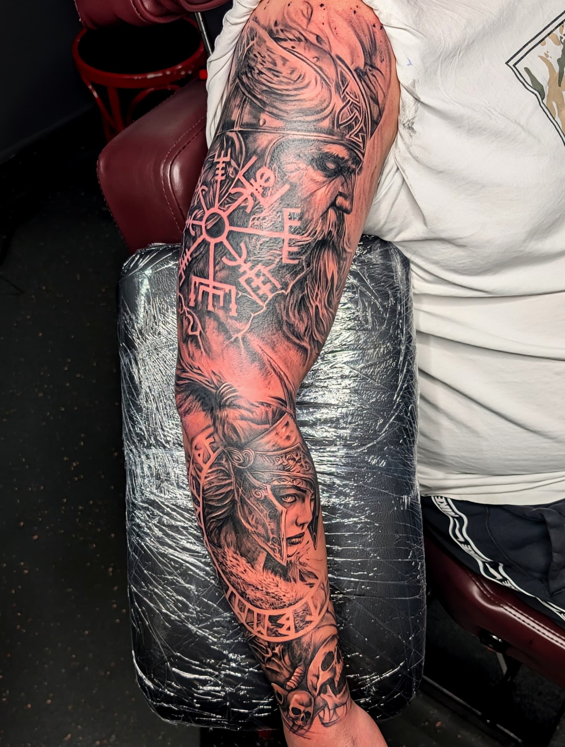 Black and grey realism tattoo of Viking warriors, runes and skulls covering the full arm
