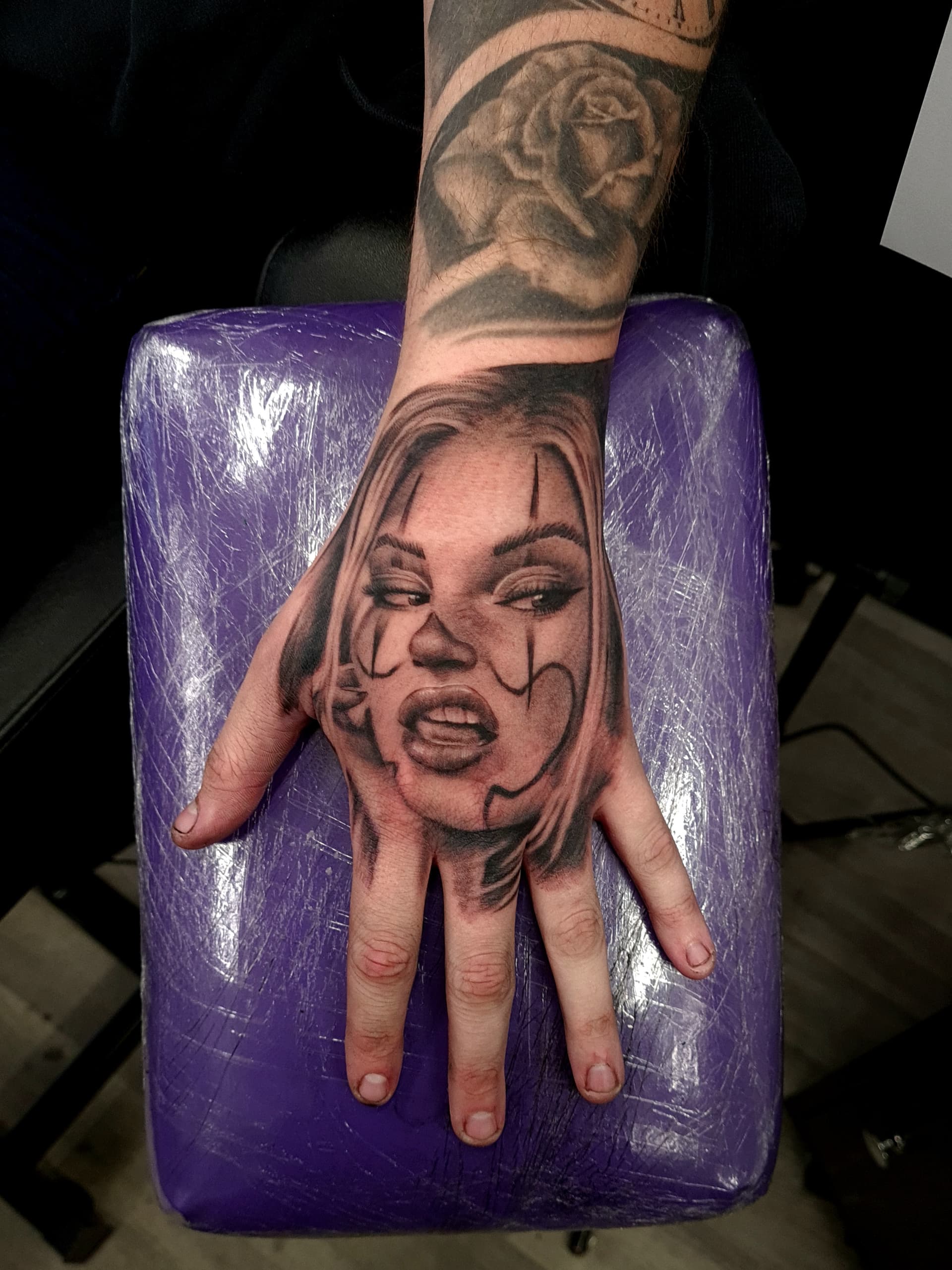 Black and grey realism tattoo of a woman's face with clown makeup on the back of the hand