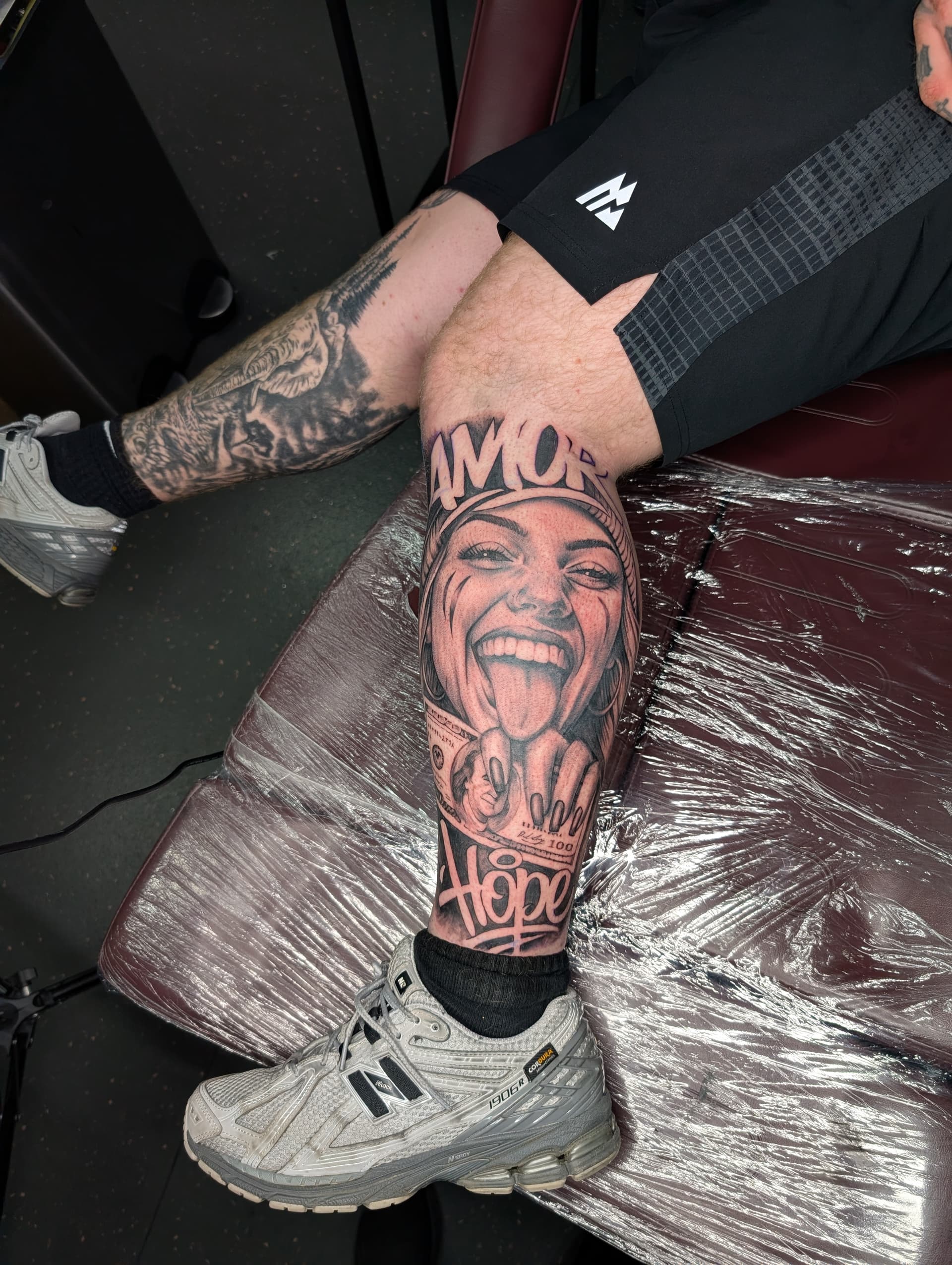 Black and grey realism tattoo of a laughing woman's face with money and script lettering on the lower leg