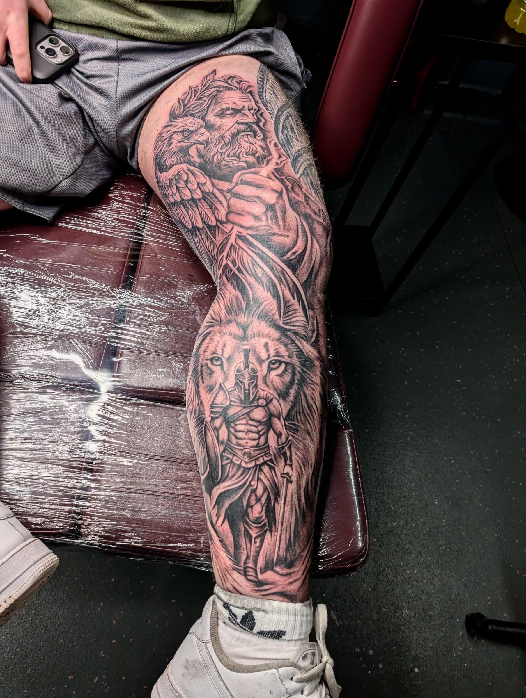 Black and grey realism leg sleeve tattoo featuring Zeus, an eagle, a wolf and a Spartan warrior
